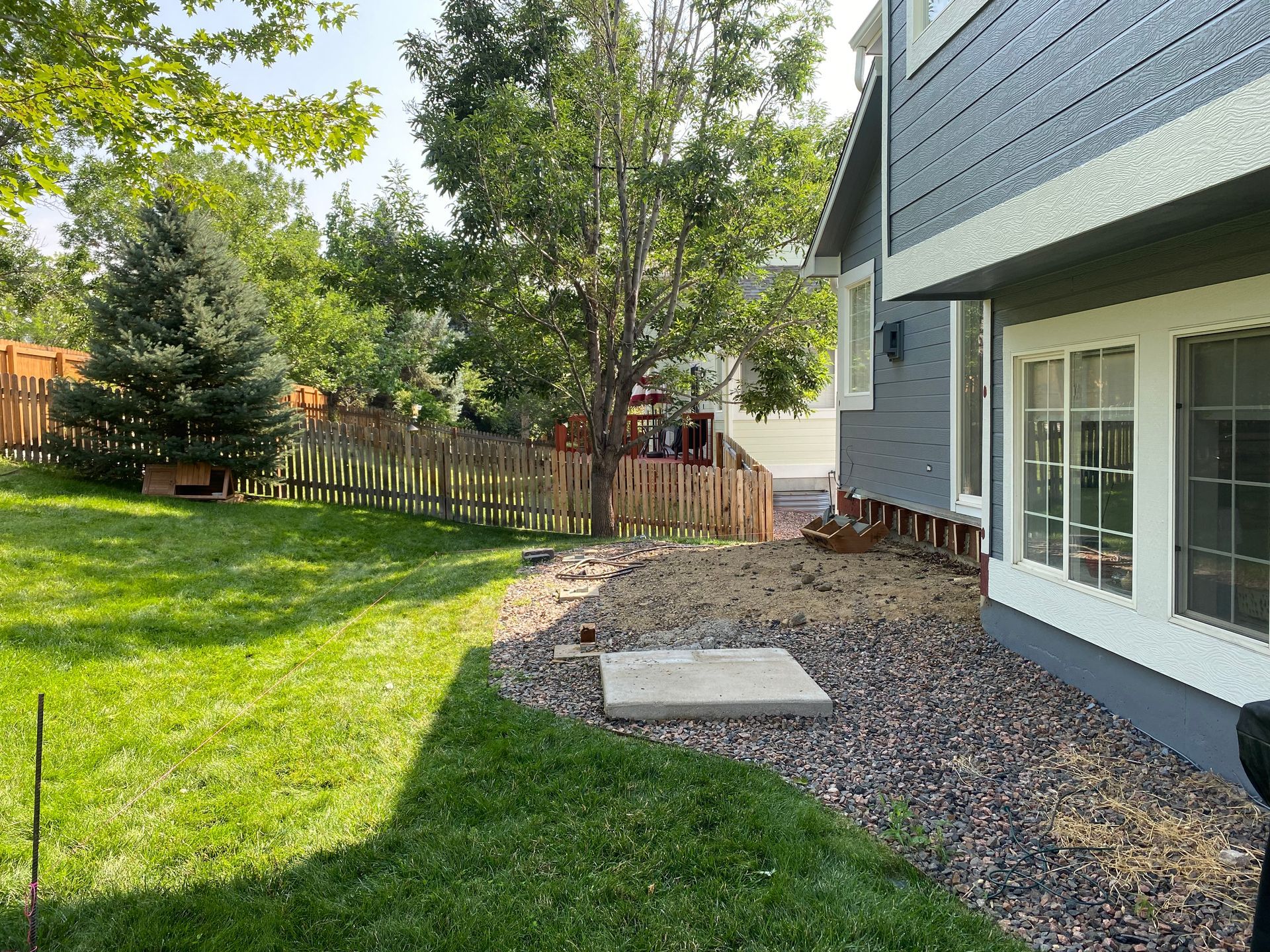 Backyard with green grass, brown fence, and a gray house.