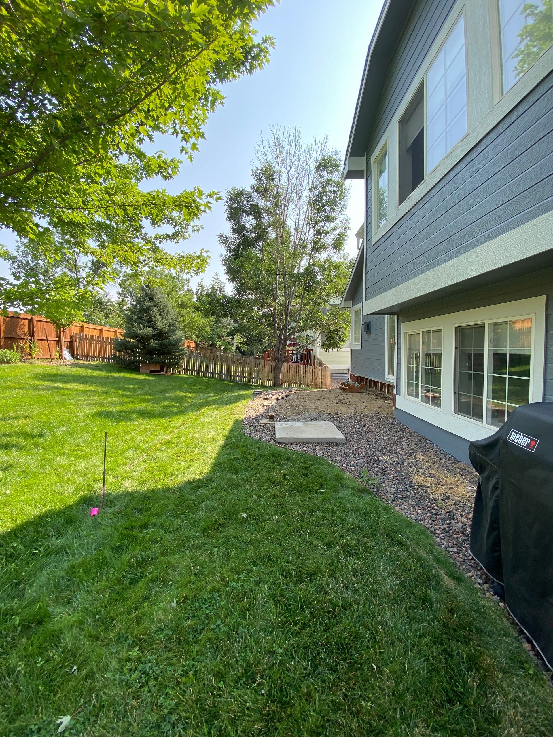 Backyard with green grass, trees, and a house with blue siding.
