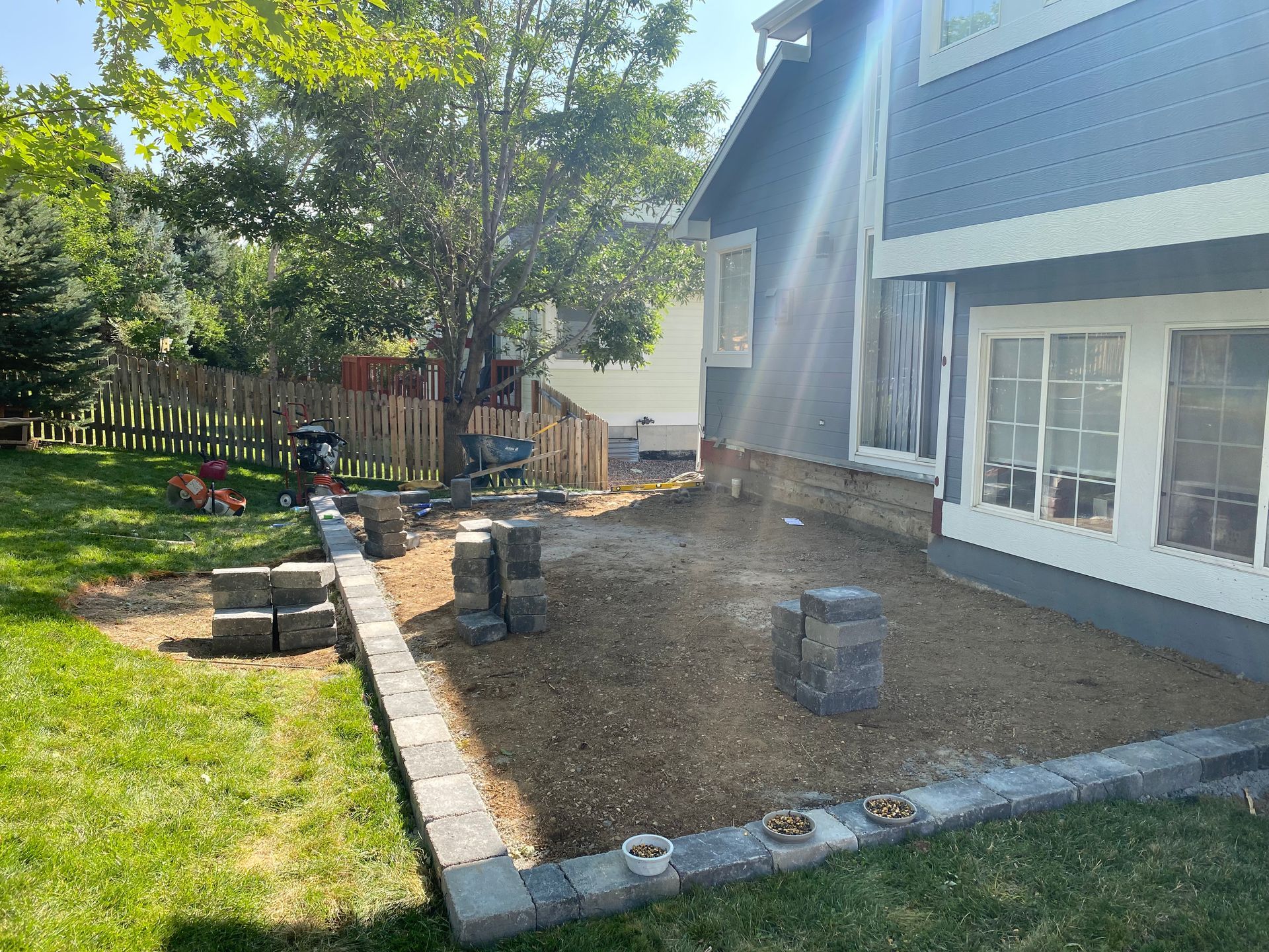Backyard with a stone retaining wall and small garden area next to a blue house on a sunny day.