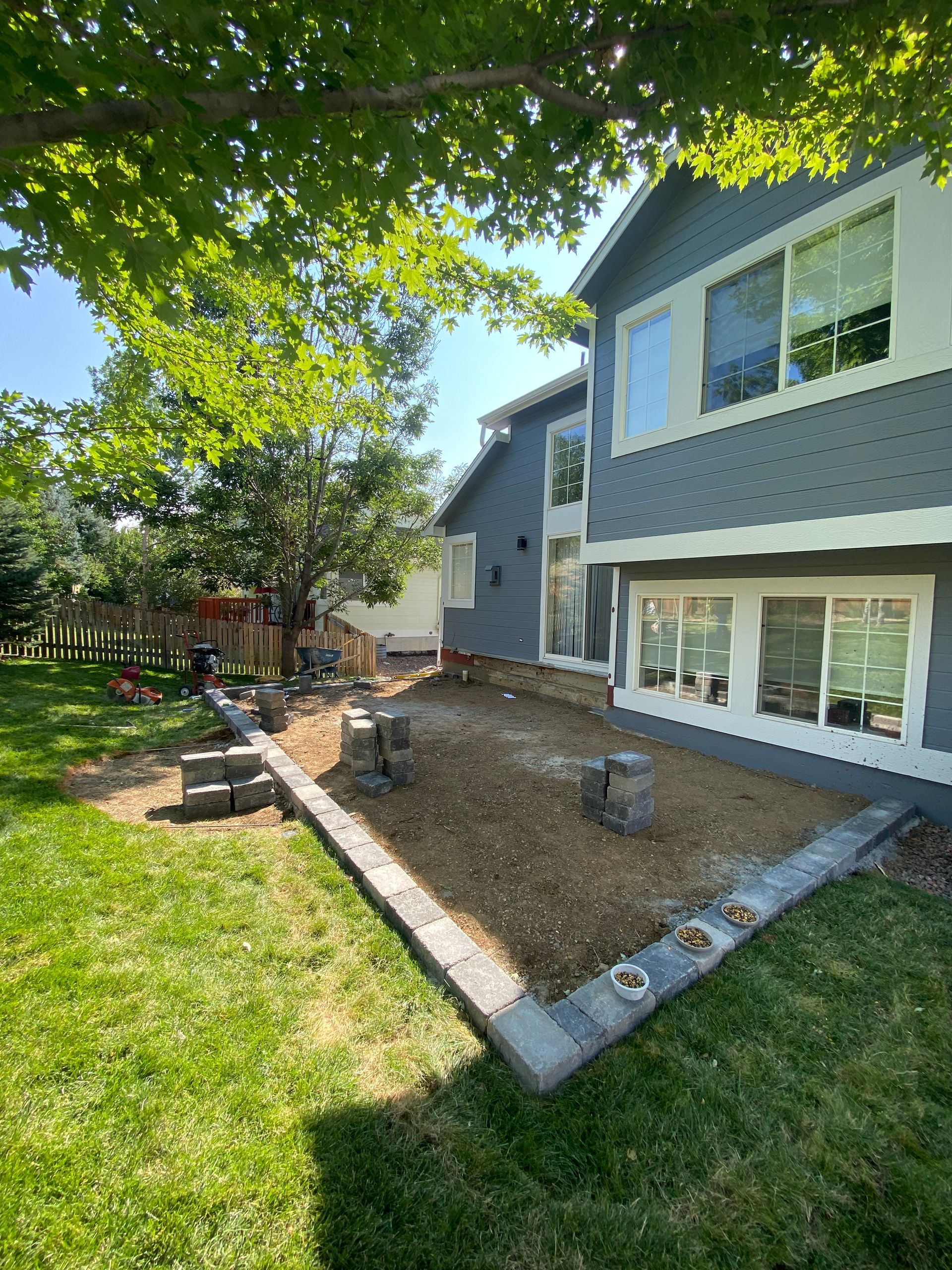 Backyard landscaping with a retaining wall, newly seeded area, and a two-story blue house.