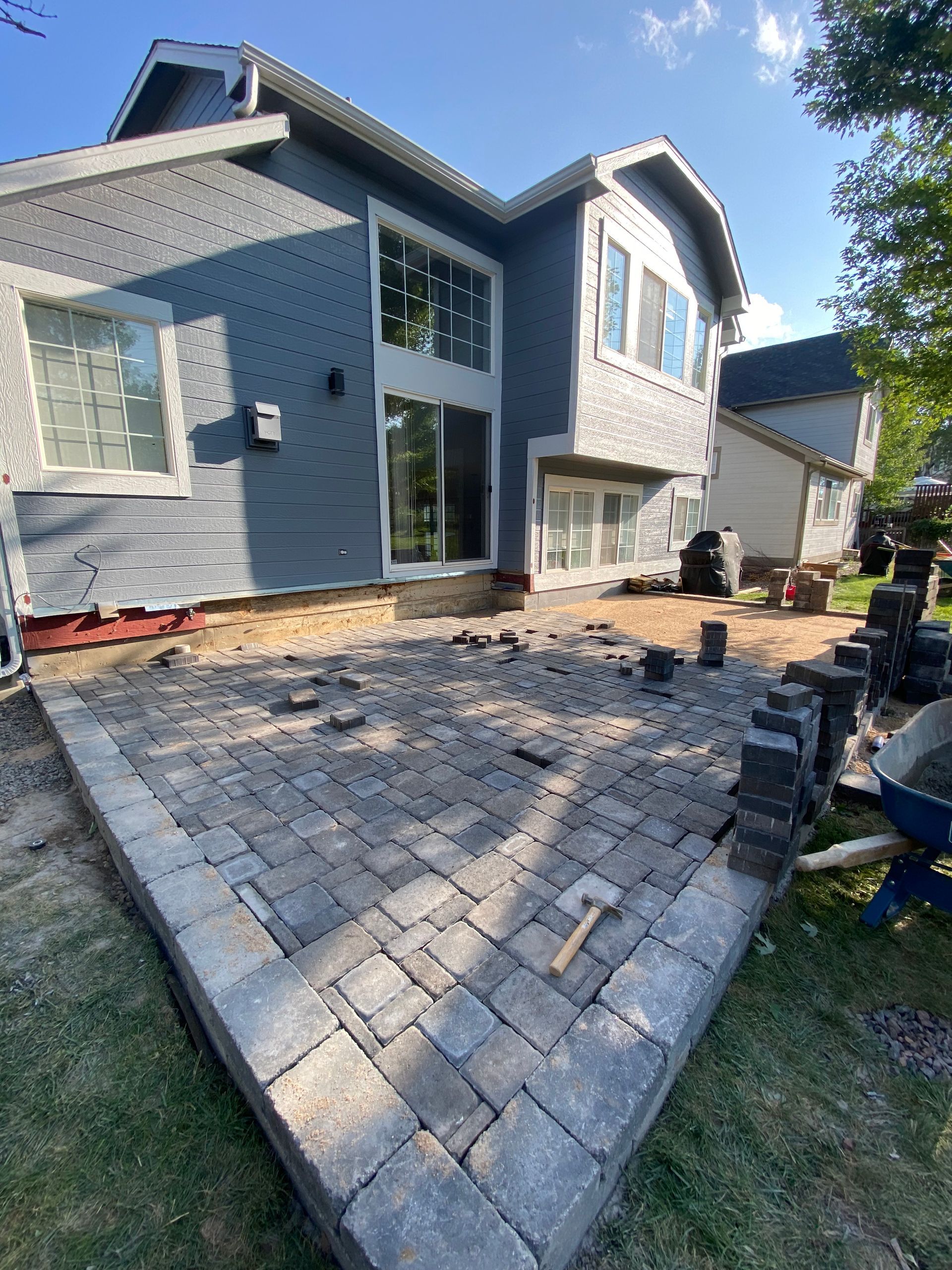 Backyard patio under construction with gray pavers, house in background.