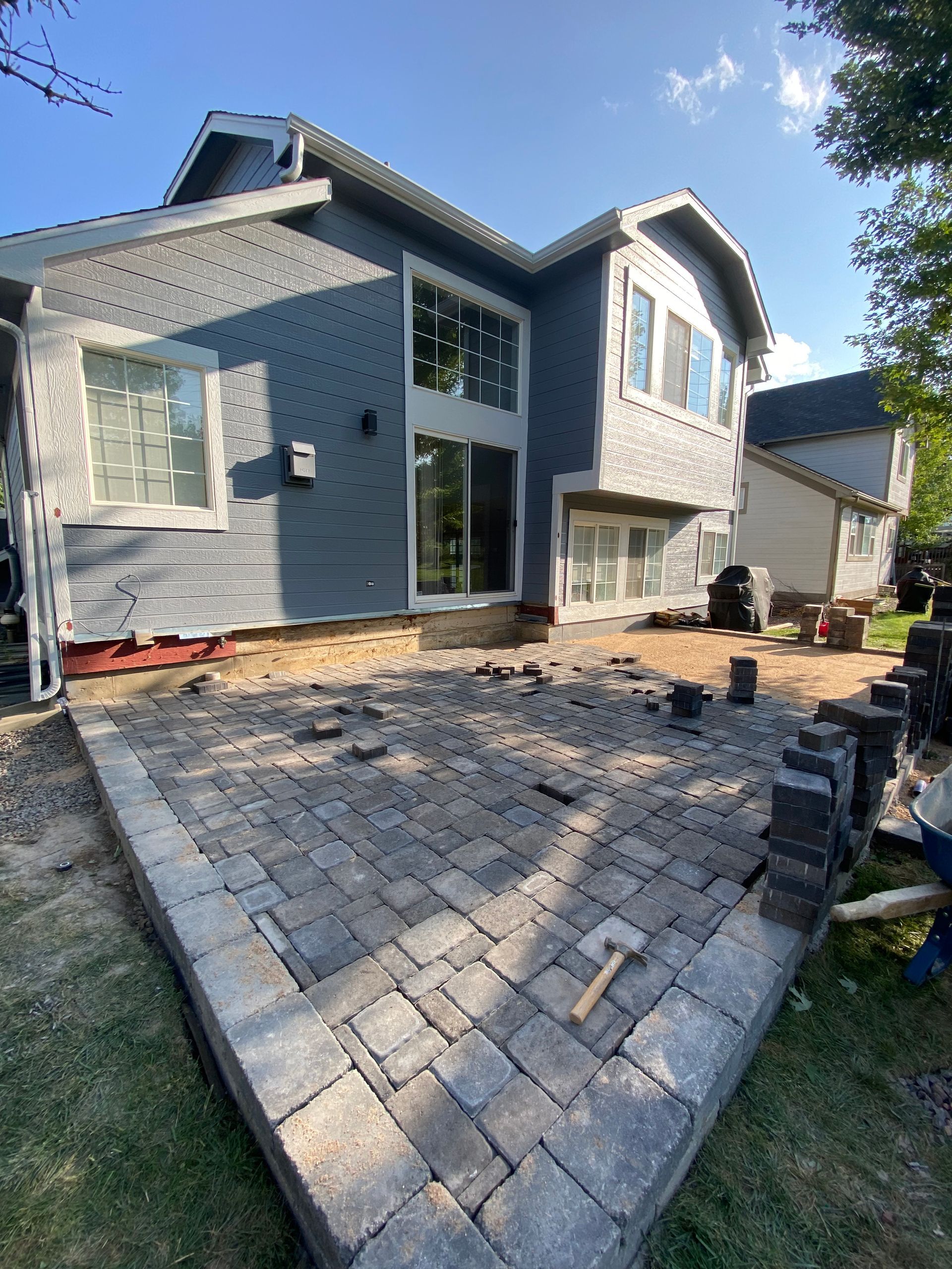 A patio being built with gray pavers next to a two-story gray house.