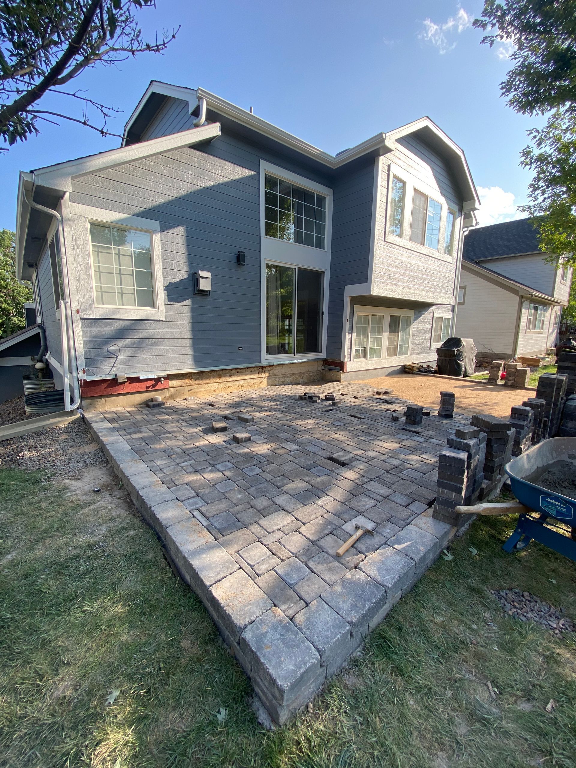 Back of gray house with new patio under construction; blue sky.