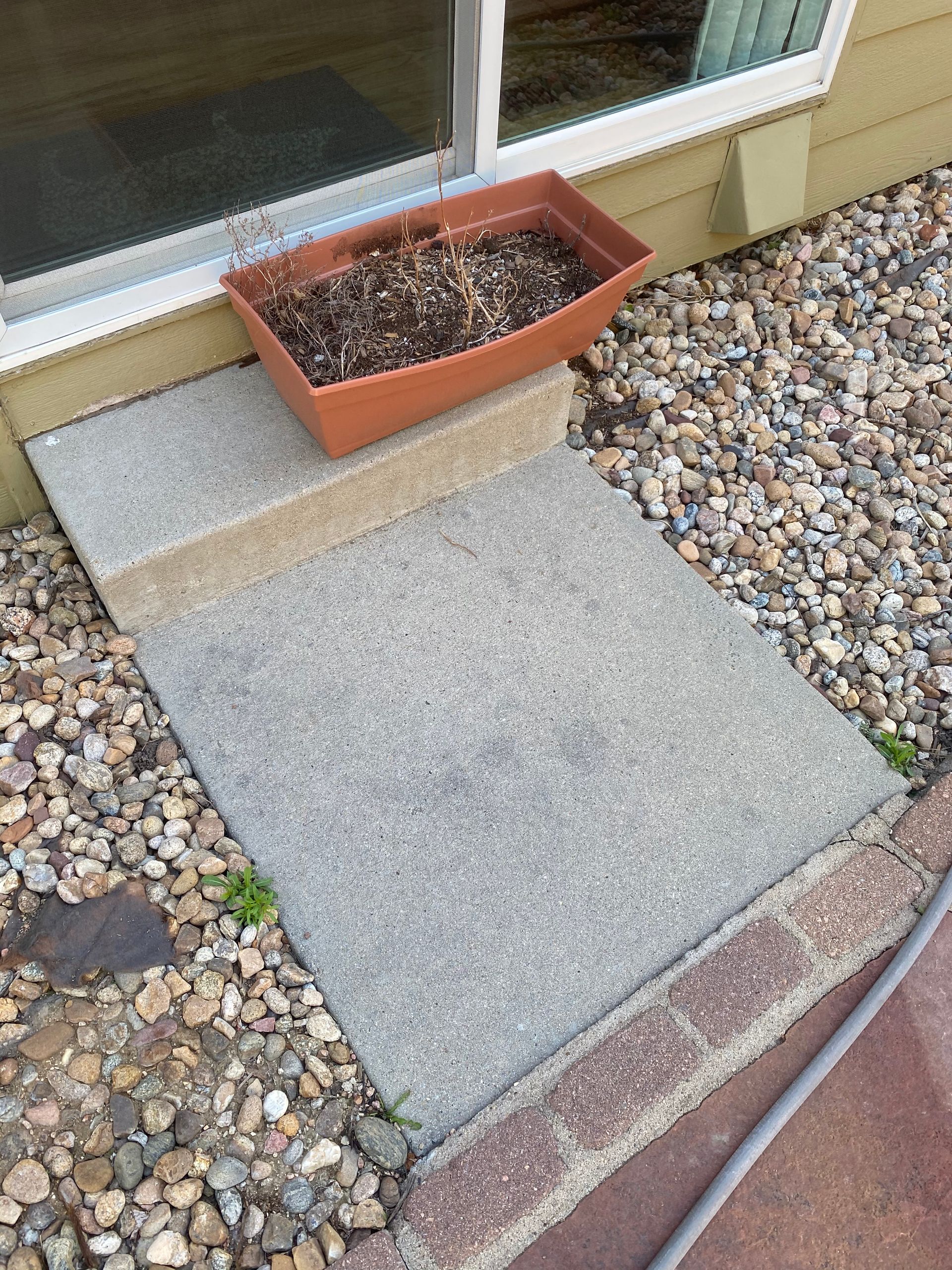 Concrete steps leading up to a sliding glass door, with a planter box and gravel.