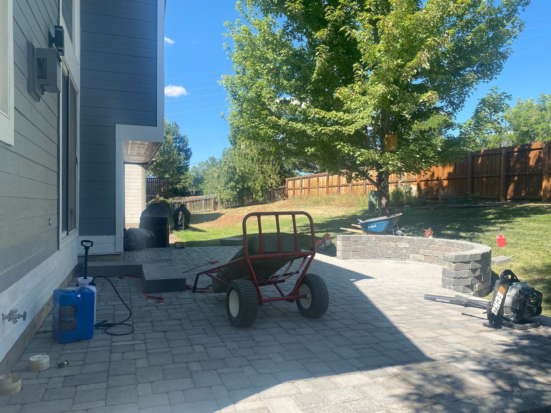 Backyard with brick patio, a red wagon, and a fire pit near a house.