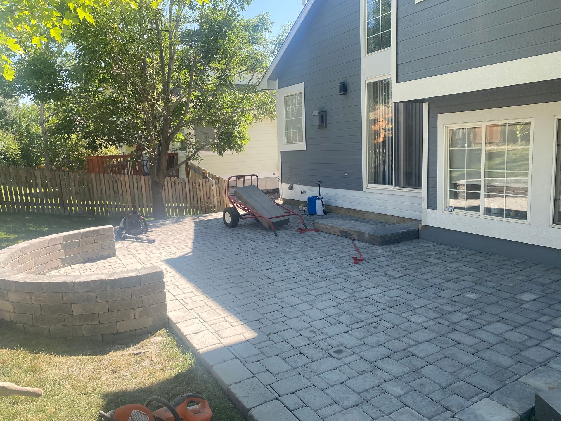 Backyard patio with gray pavers, curved retaining wall, and house with gray siding.