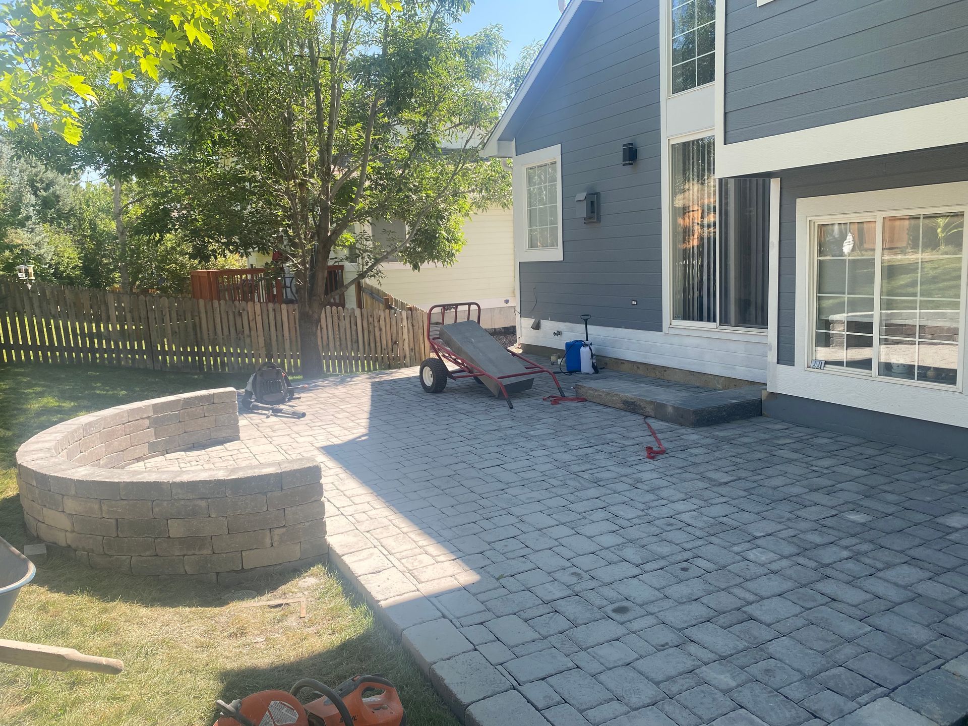 Backyard patio with grey pavers, curved stone seating, and a two-story grey house.