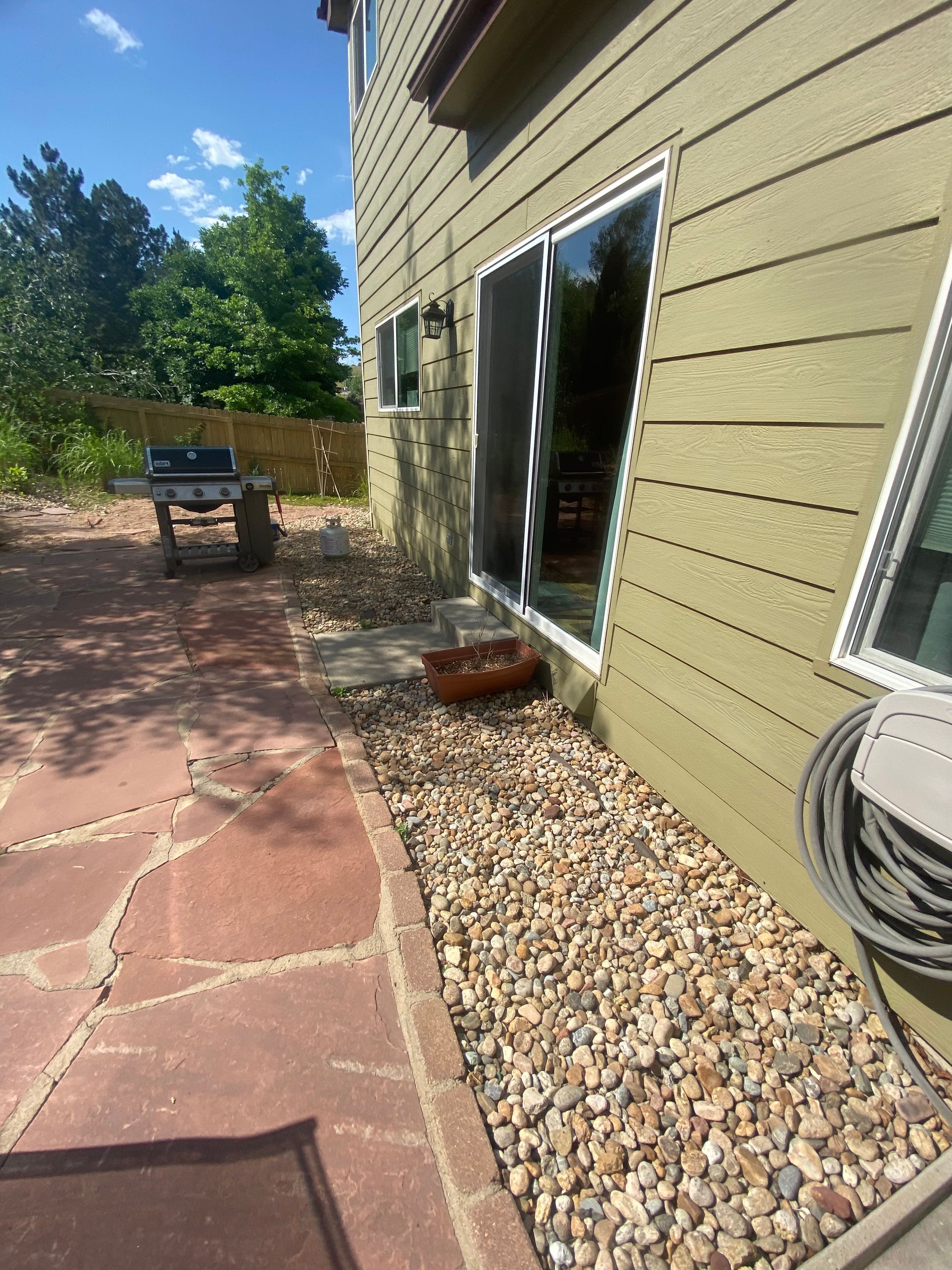Backyard with sliding glass door, rocks, and a grill on a sunny day.