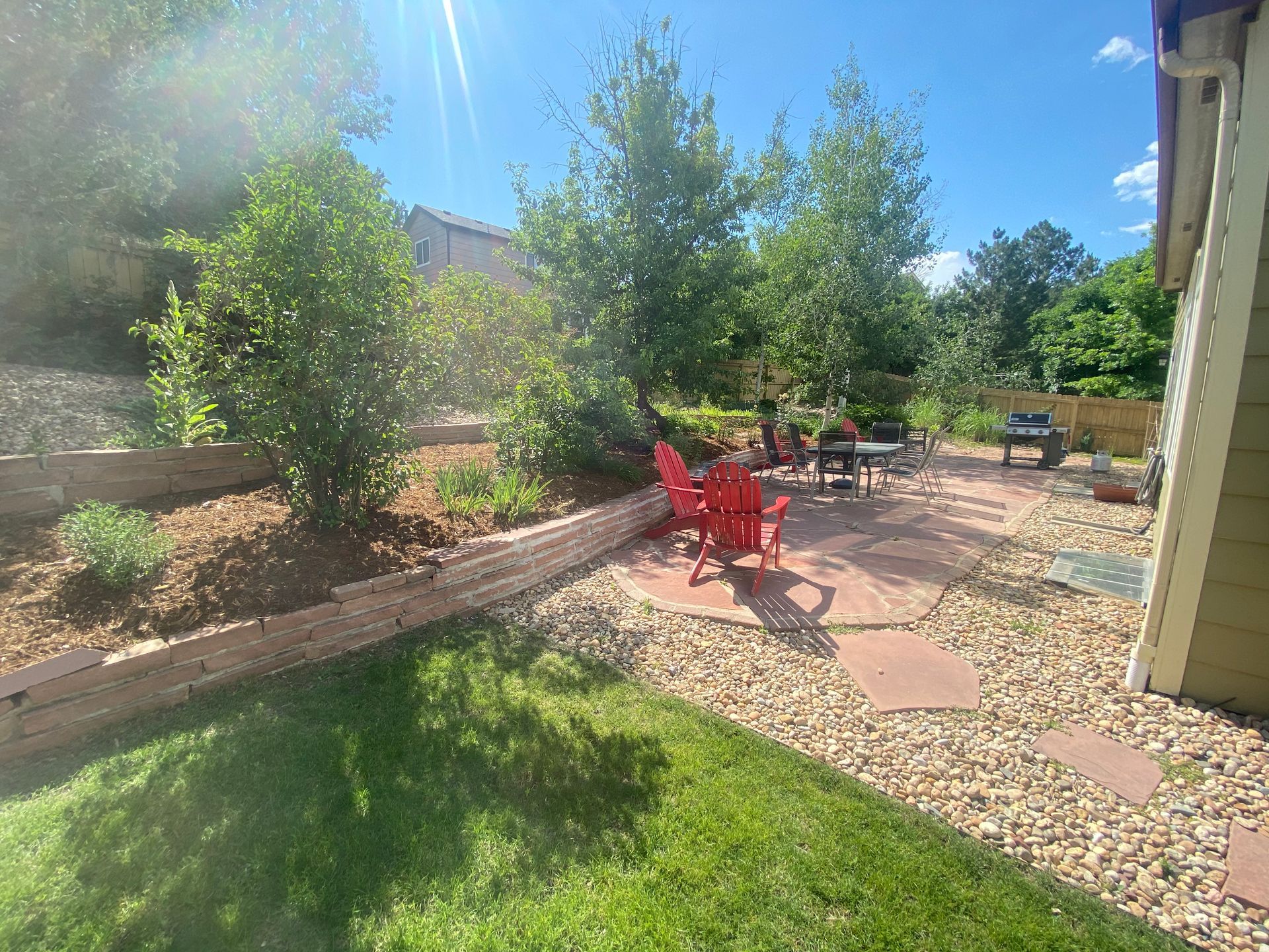 Red chairs on a patio with trees and a green lawn on a sunny day.