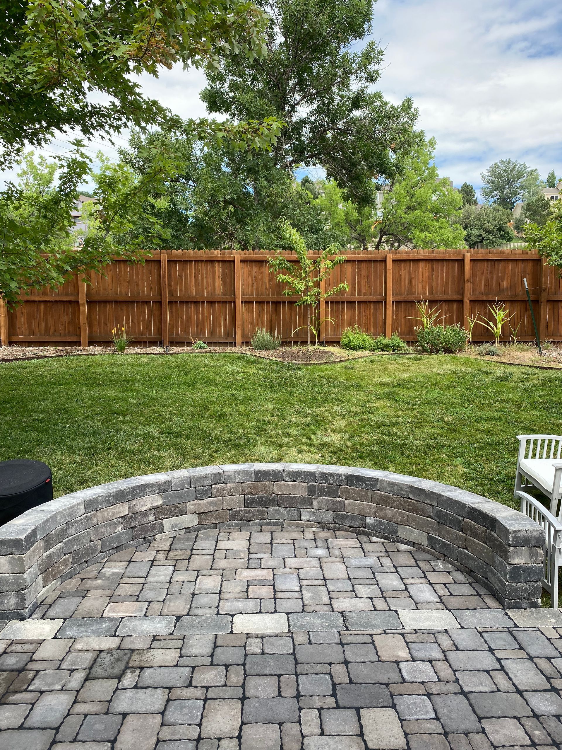 A curved brick patio with a grass yard and wooden fence in the background.