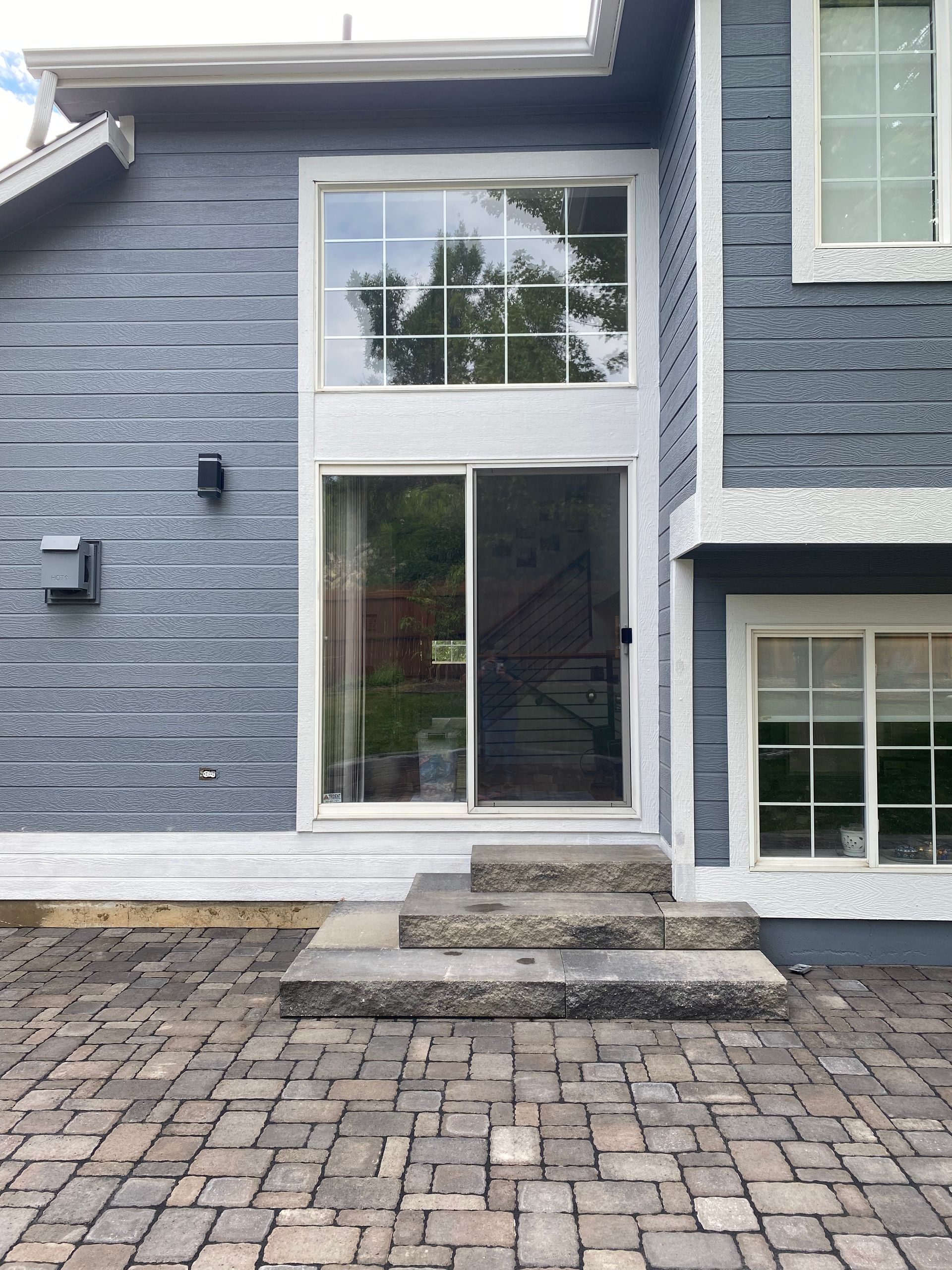 Exterior view of a house with a large window, sliding door, stone steps, and brick patio.
