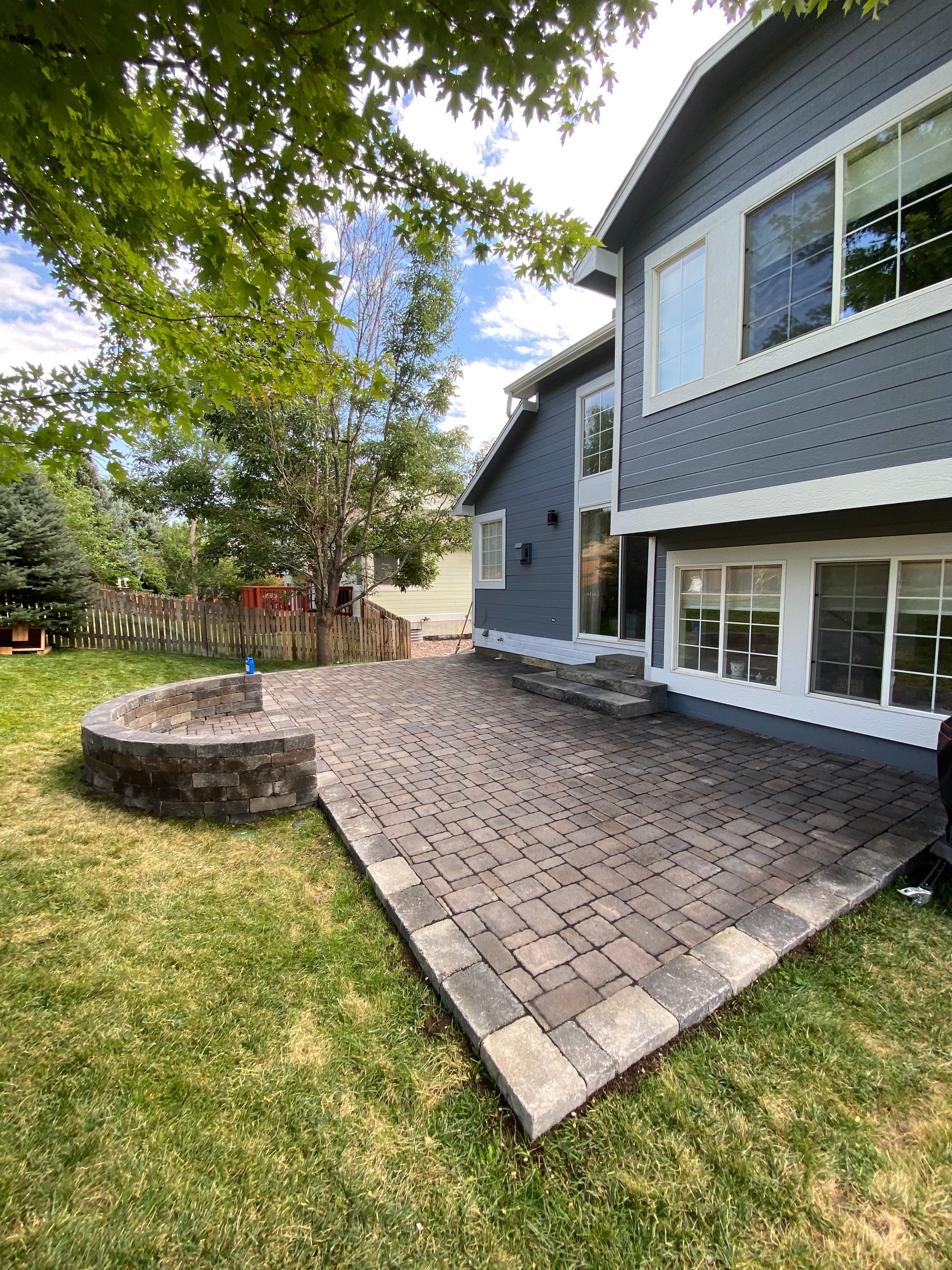 A backyard with a brick patio, fire pit, and a two-story gray house.