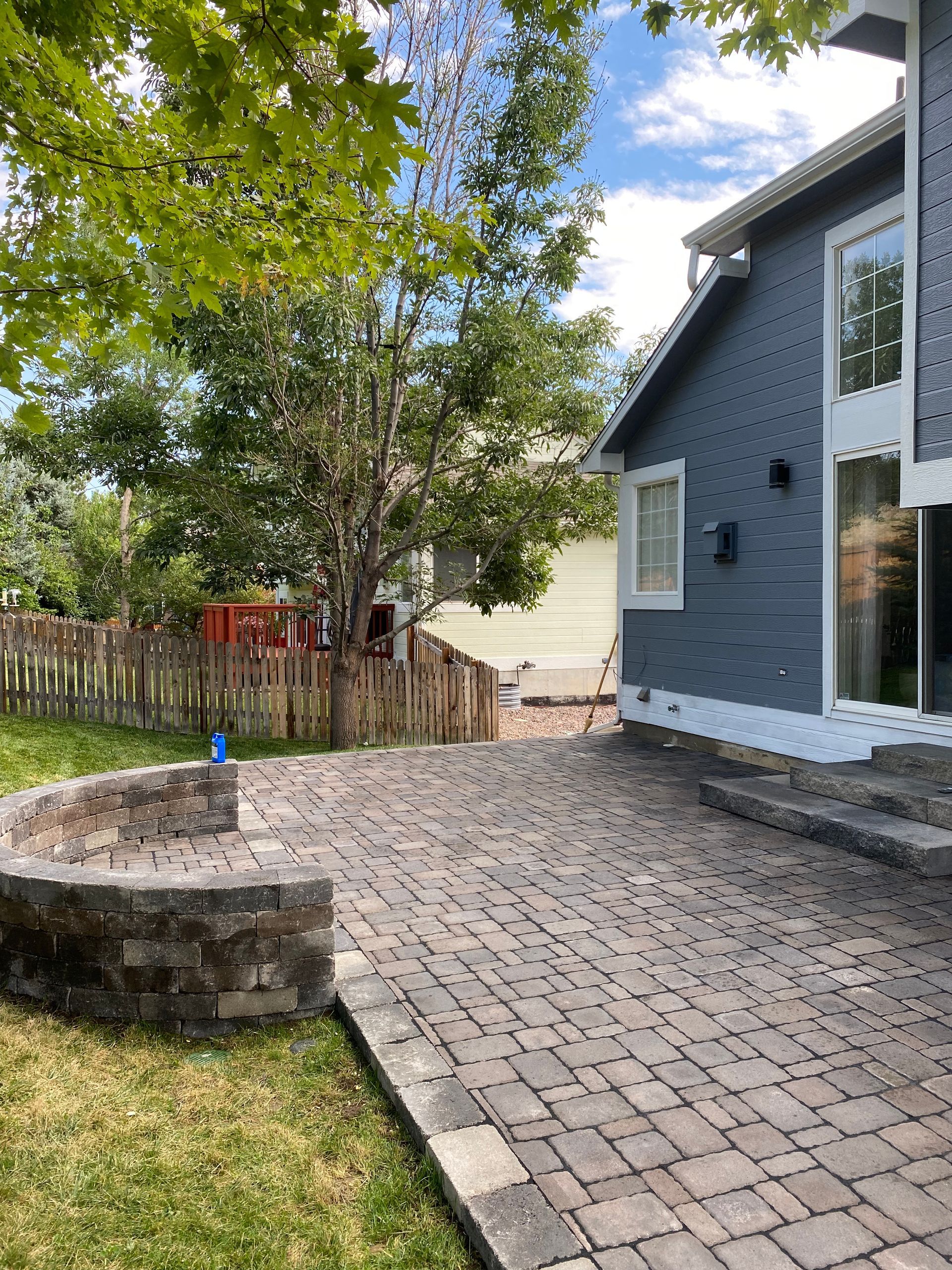 Patio with brick pavers, low wall, and gray house on a sunny day.
