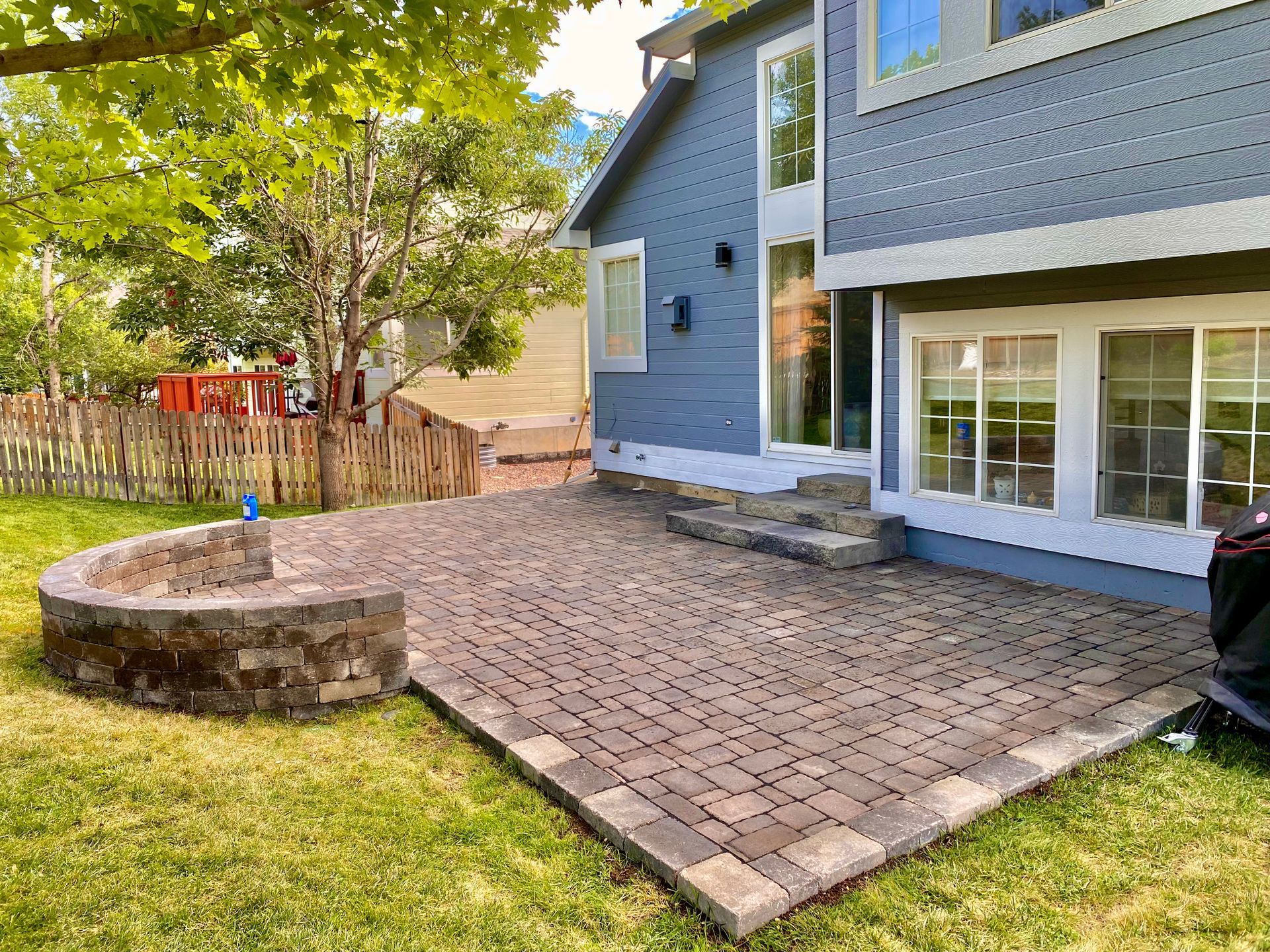 Backyard patio with brick pavers, stone fire pit, and blue house.