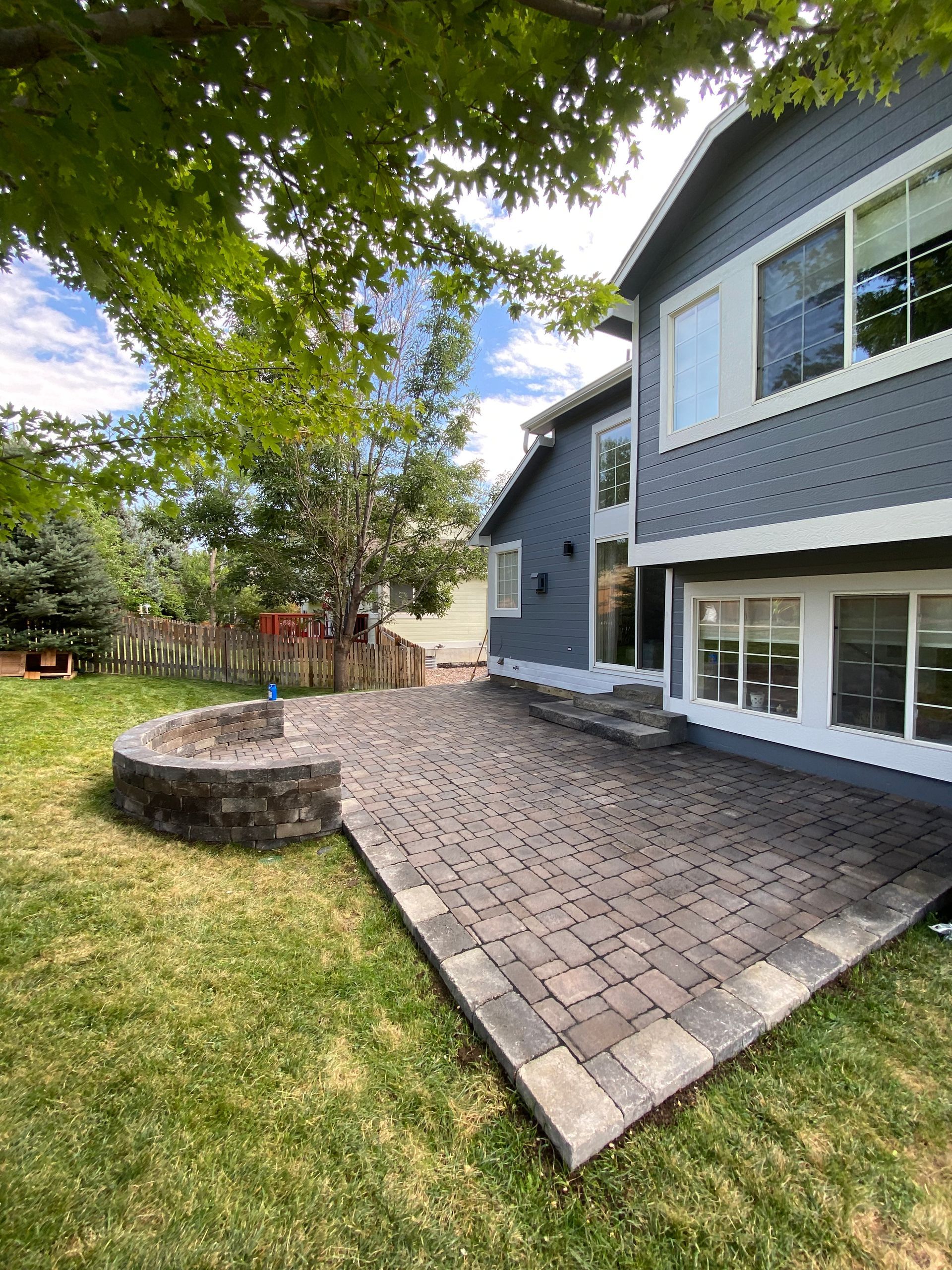 Backyard patio with brick pavers, fire pit, and a gray house with white trim.