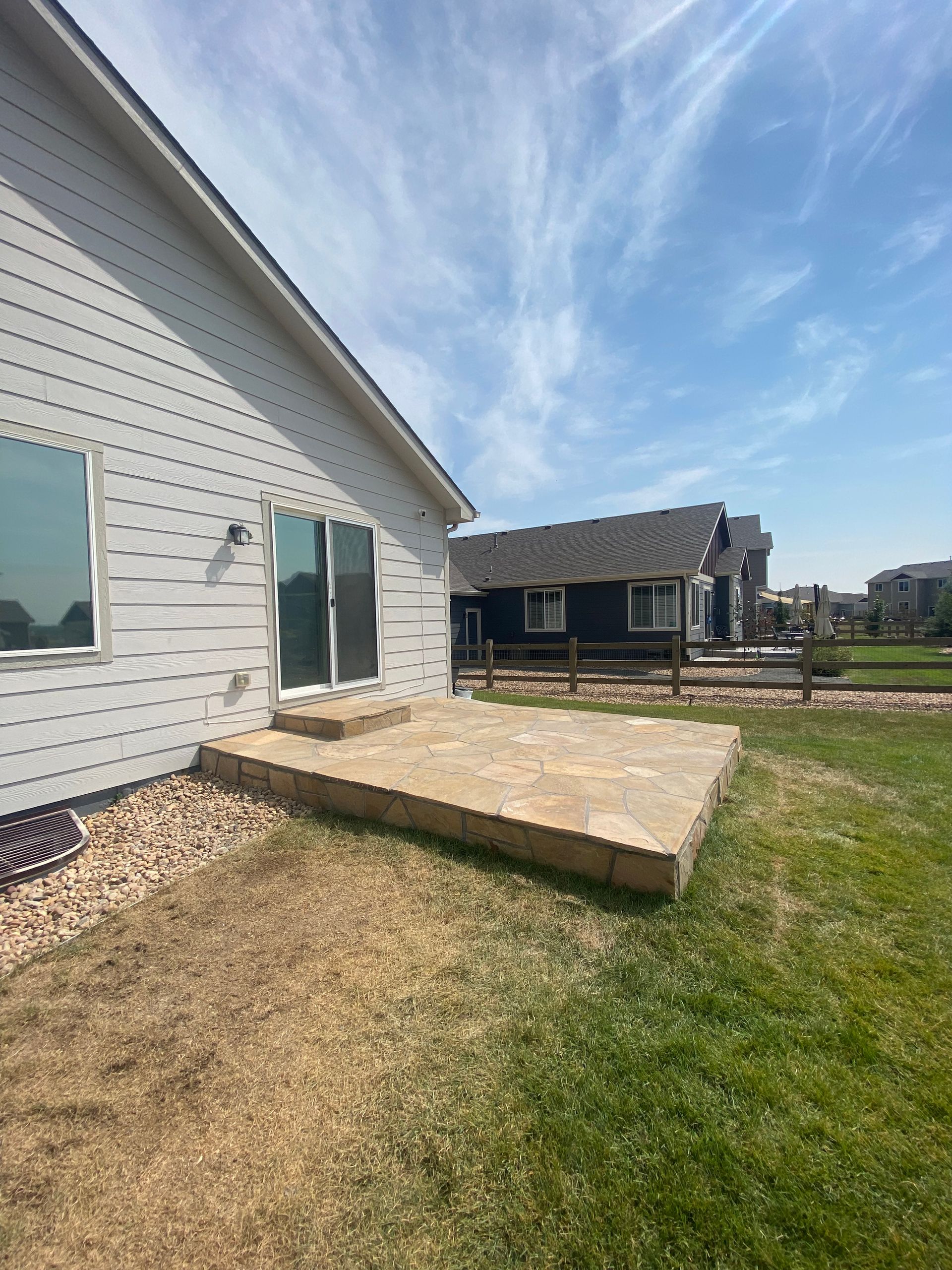 Backyard patio with sliding door, house, blue sky, and fence.
