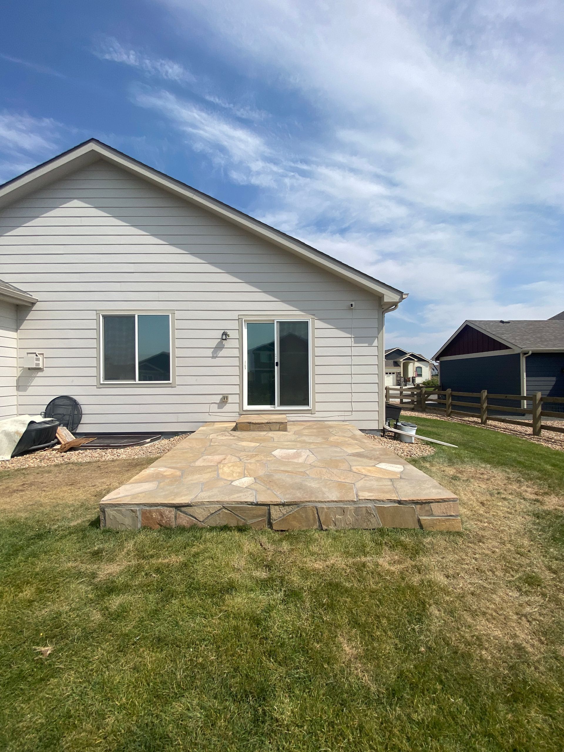 Backyard patio with stone pavers, sliding door, and green grass on a sunny day.