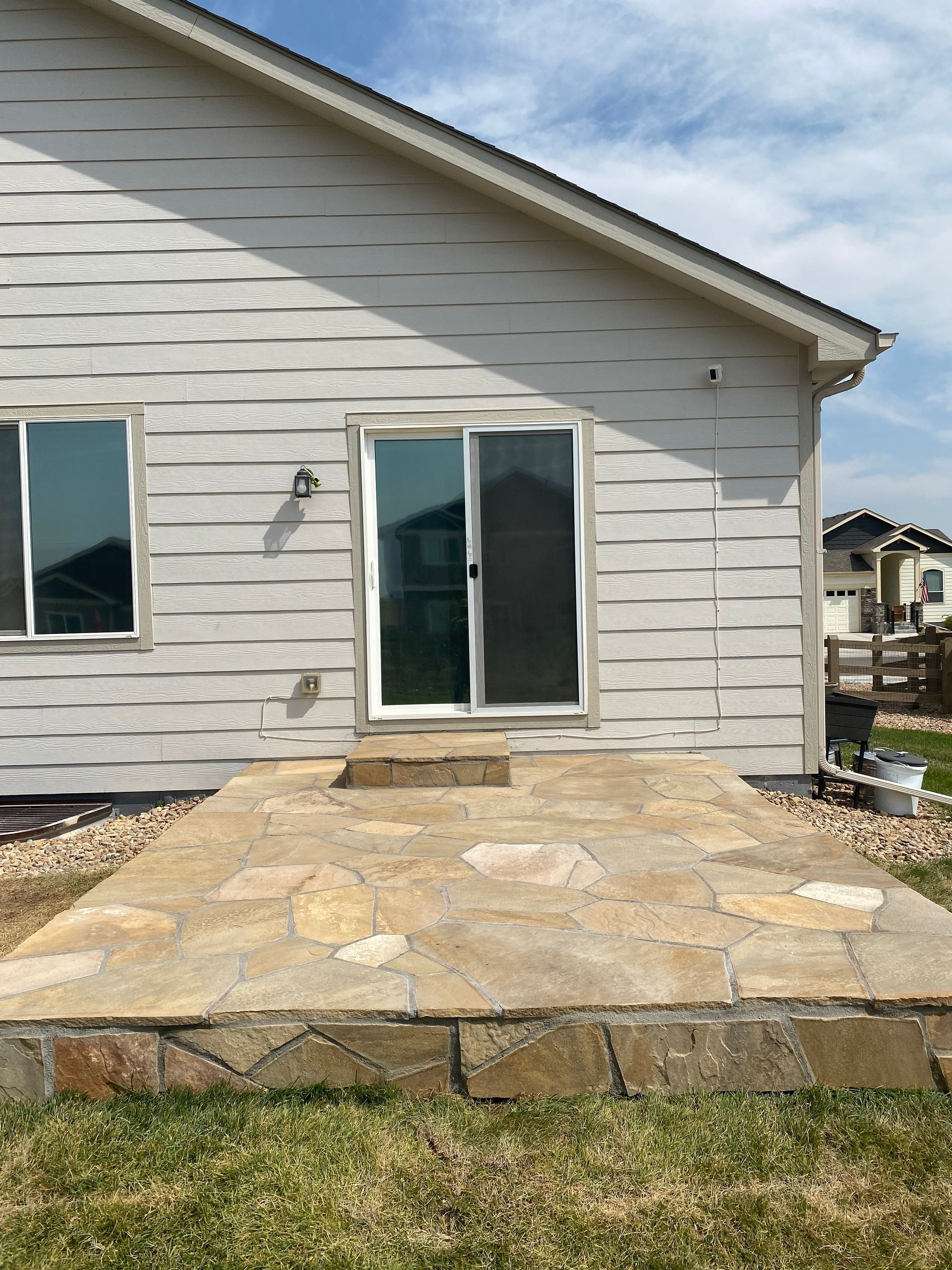 Backyard patio with flagstone, sliding glass door, and white siding.