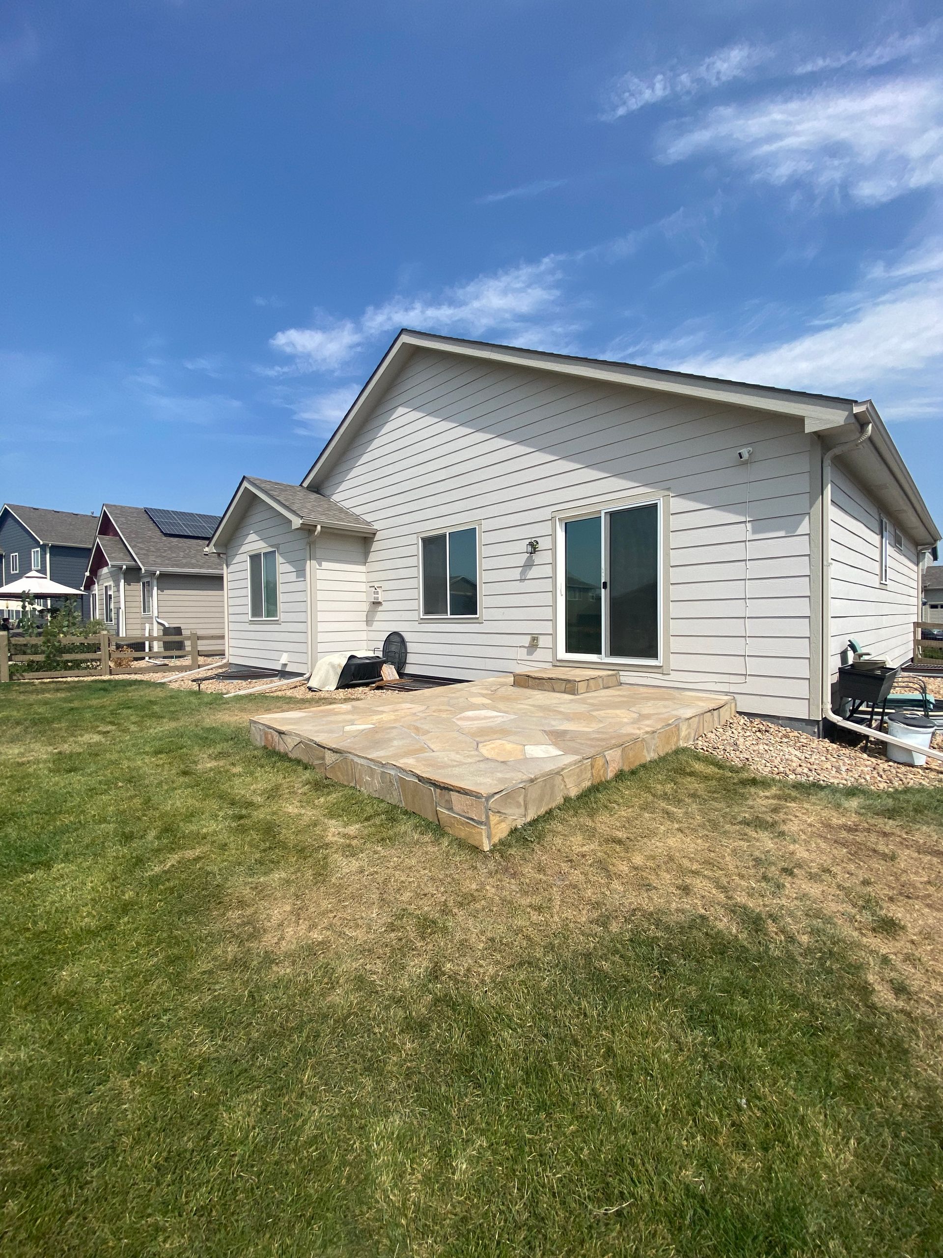 Backyard of a house with patio, green grass, and a blue sky.