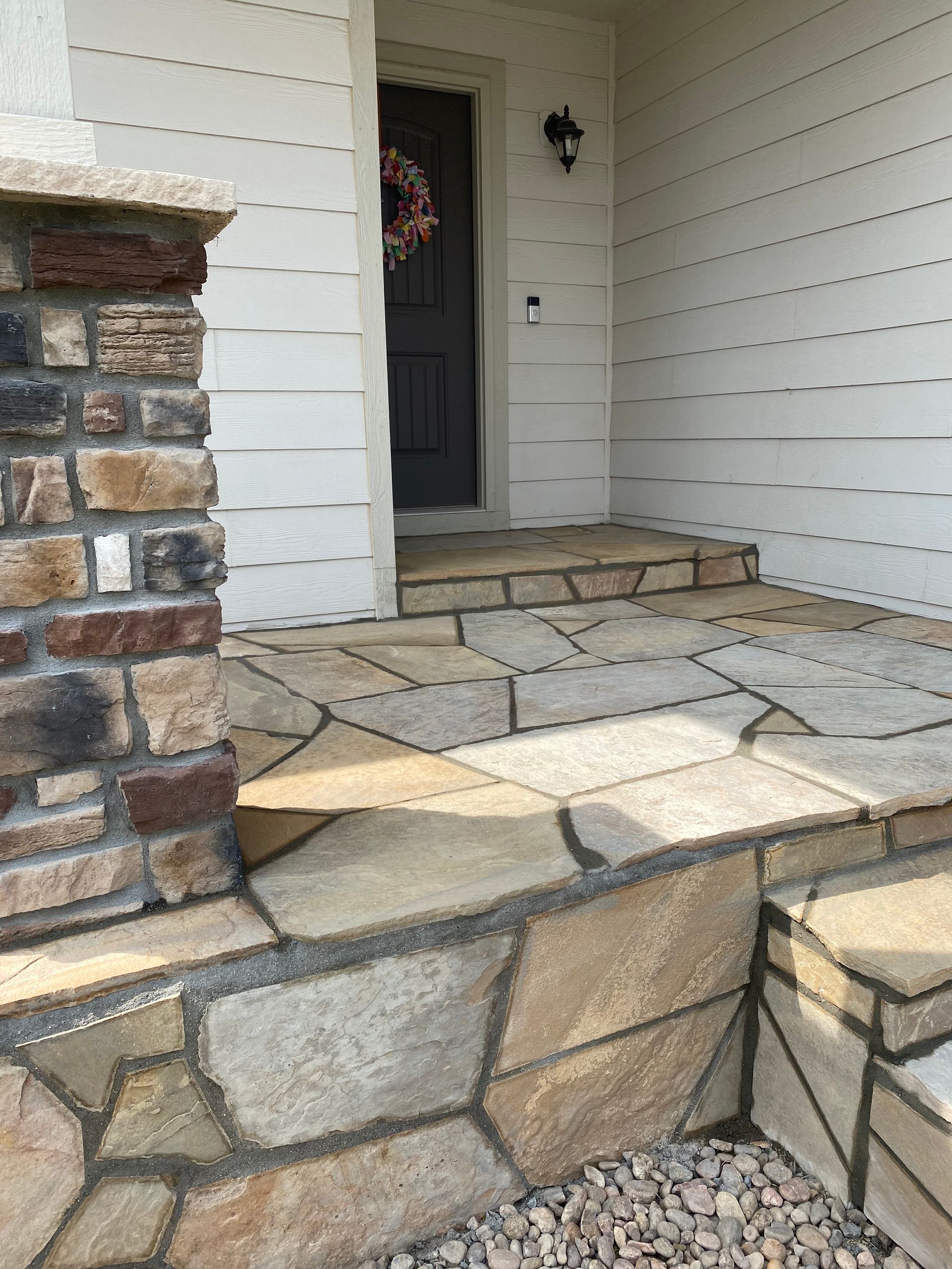 Stone walkway and steps leading to a dark front door with a wreath. A stone pillar is on the left.
