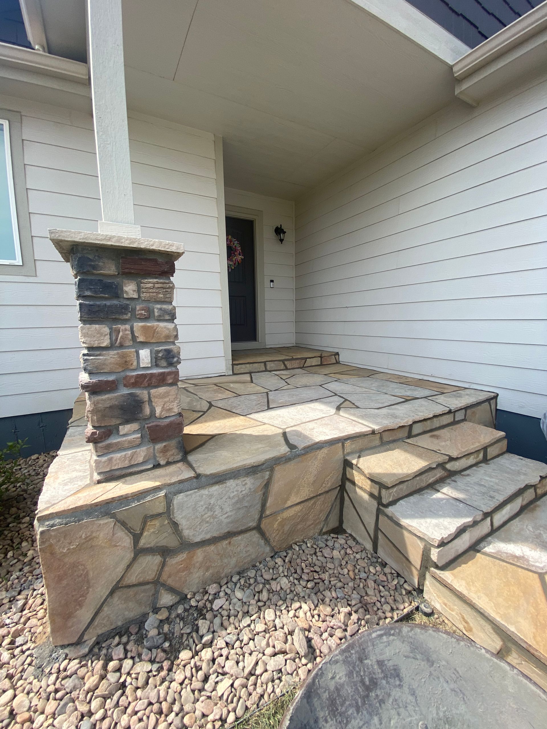 Stone steps and porch leading to a home's front door; a pillar with stone accents and a gravel base.