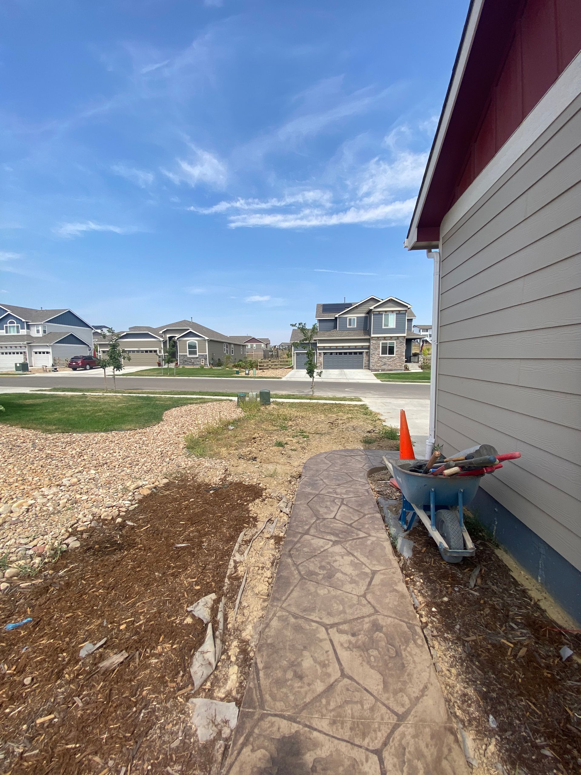 Residential neighborhood with a sidewalk under construction; wheelbarrow, blue sky.