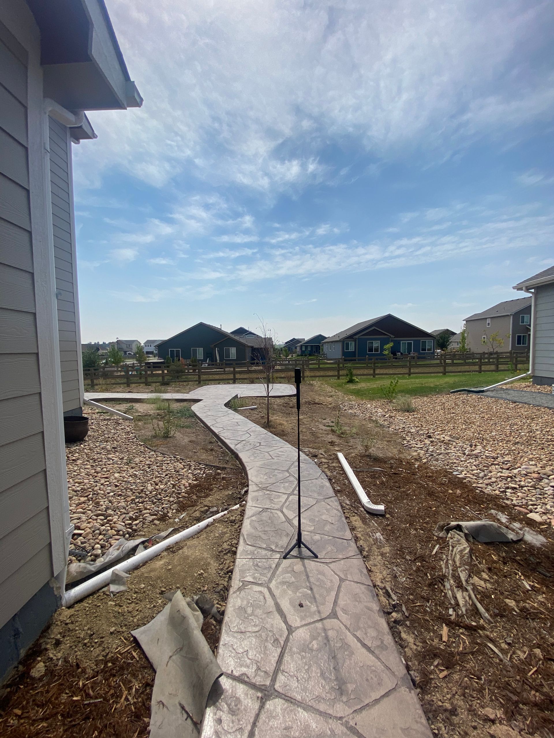Stone pathway through yard towards distant houses under a blue sky.