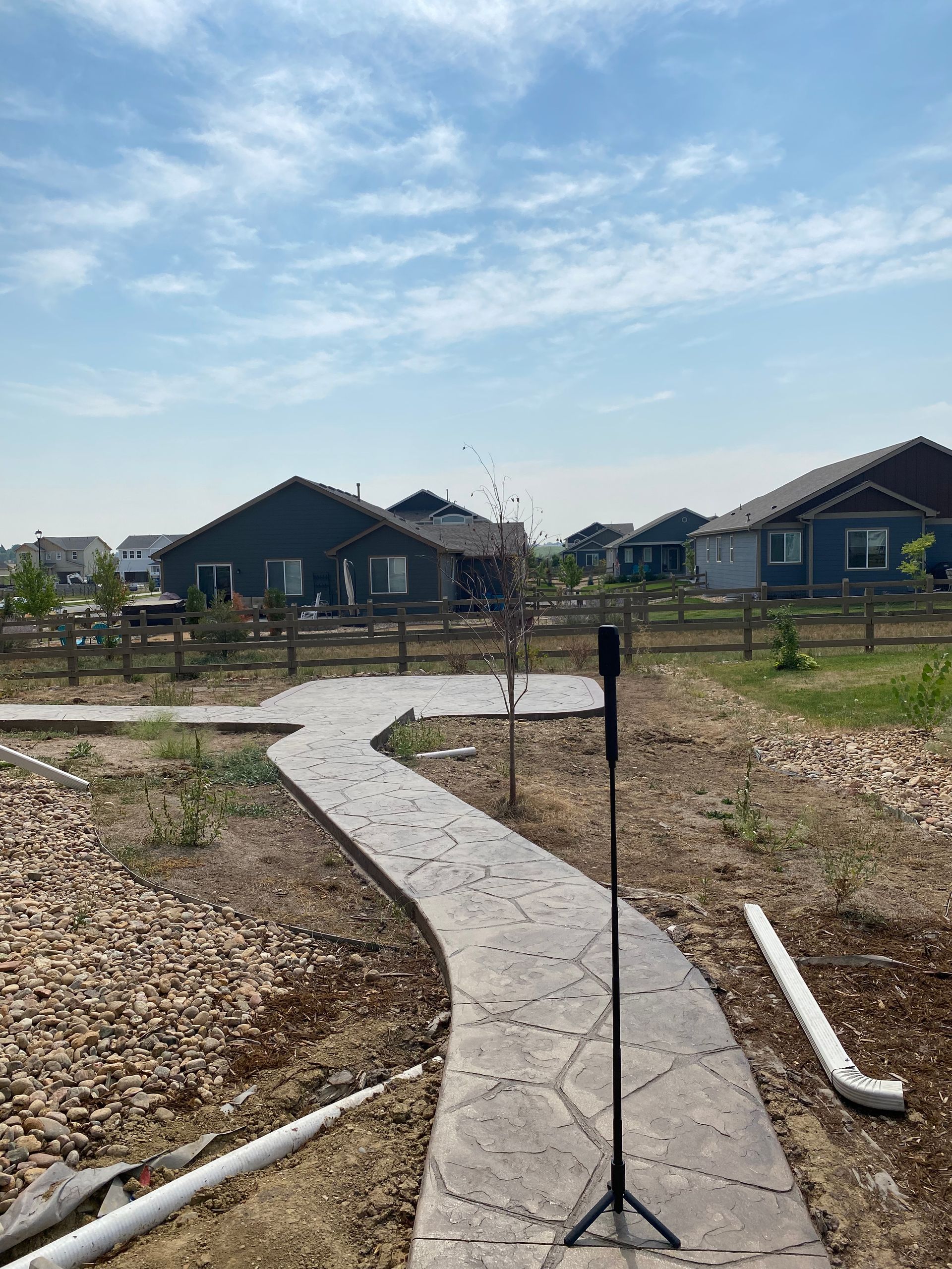A winding concrete path in a yard with houses in the background on a sunny day.