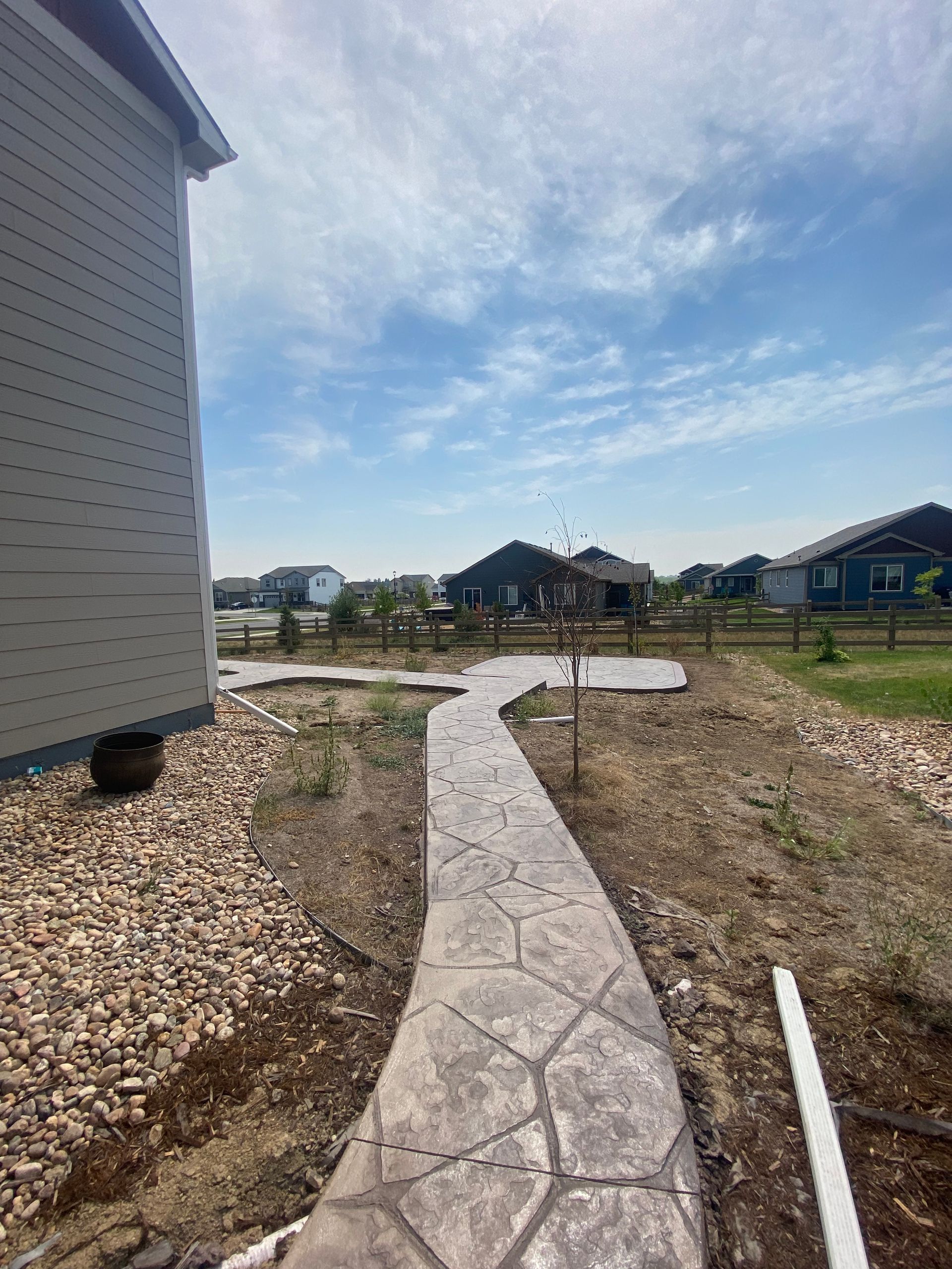 Stone walkway leading from house to open yard under a blue sky.