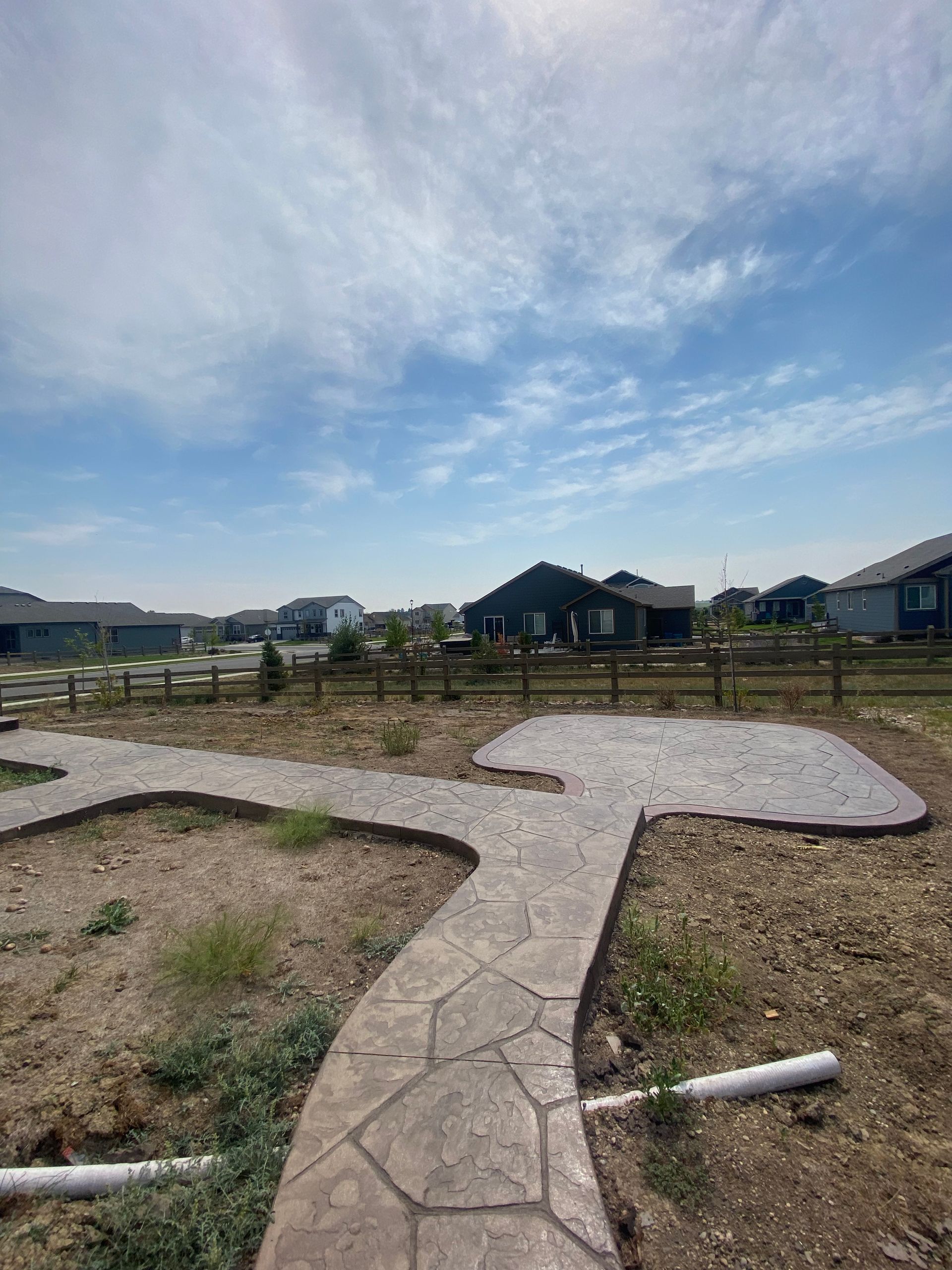 Stone path winds through a dry yard towards houses and a blue sky.