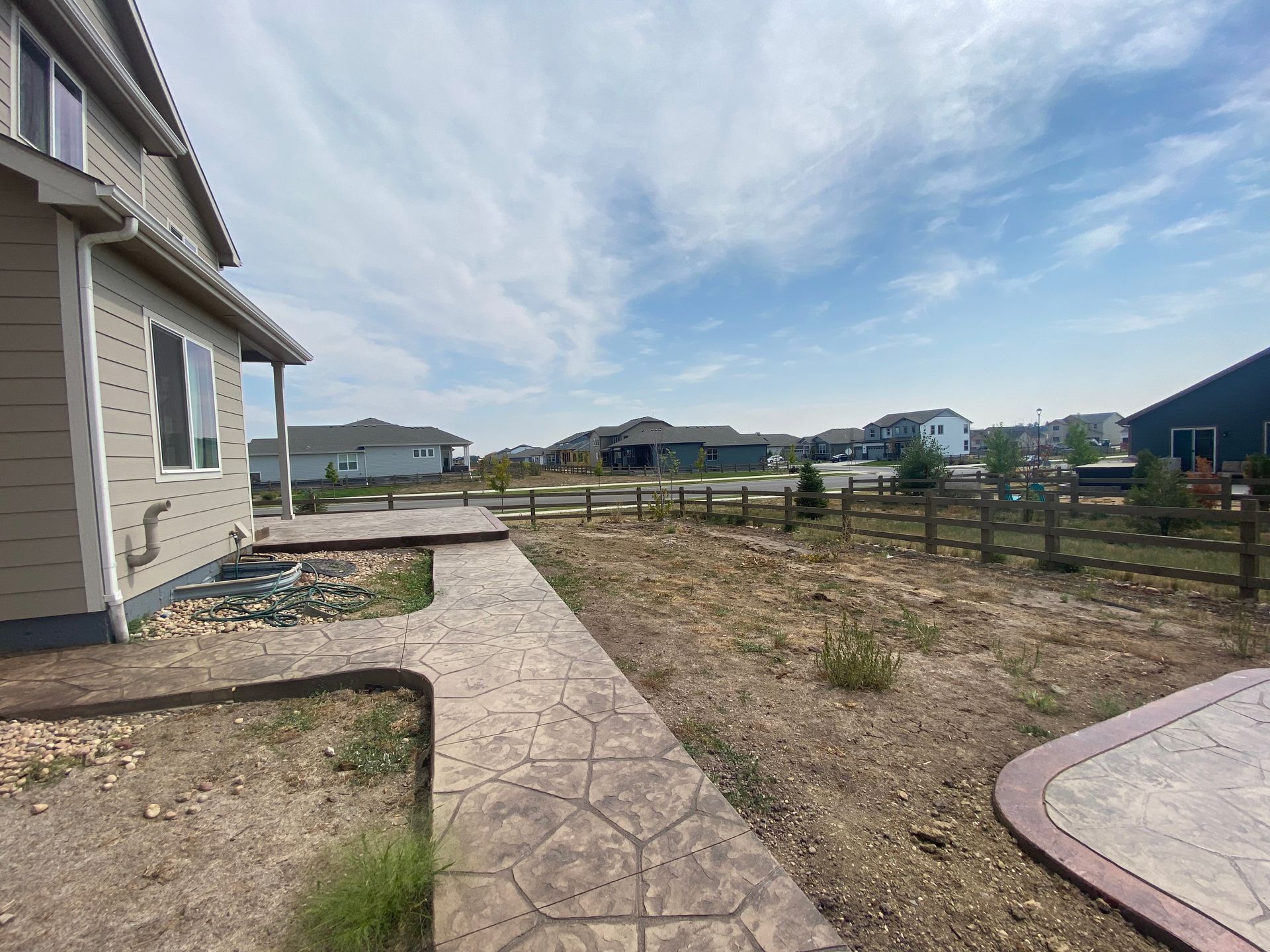 Backyard with concrete pathway, fence, houses, and cloudy sky.