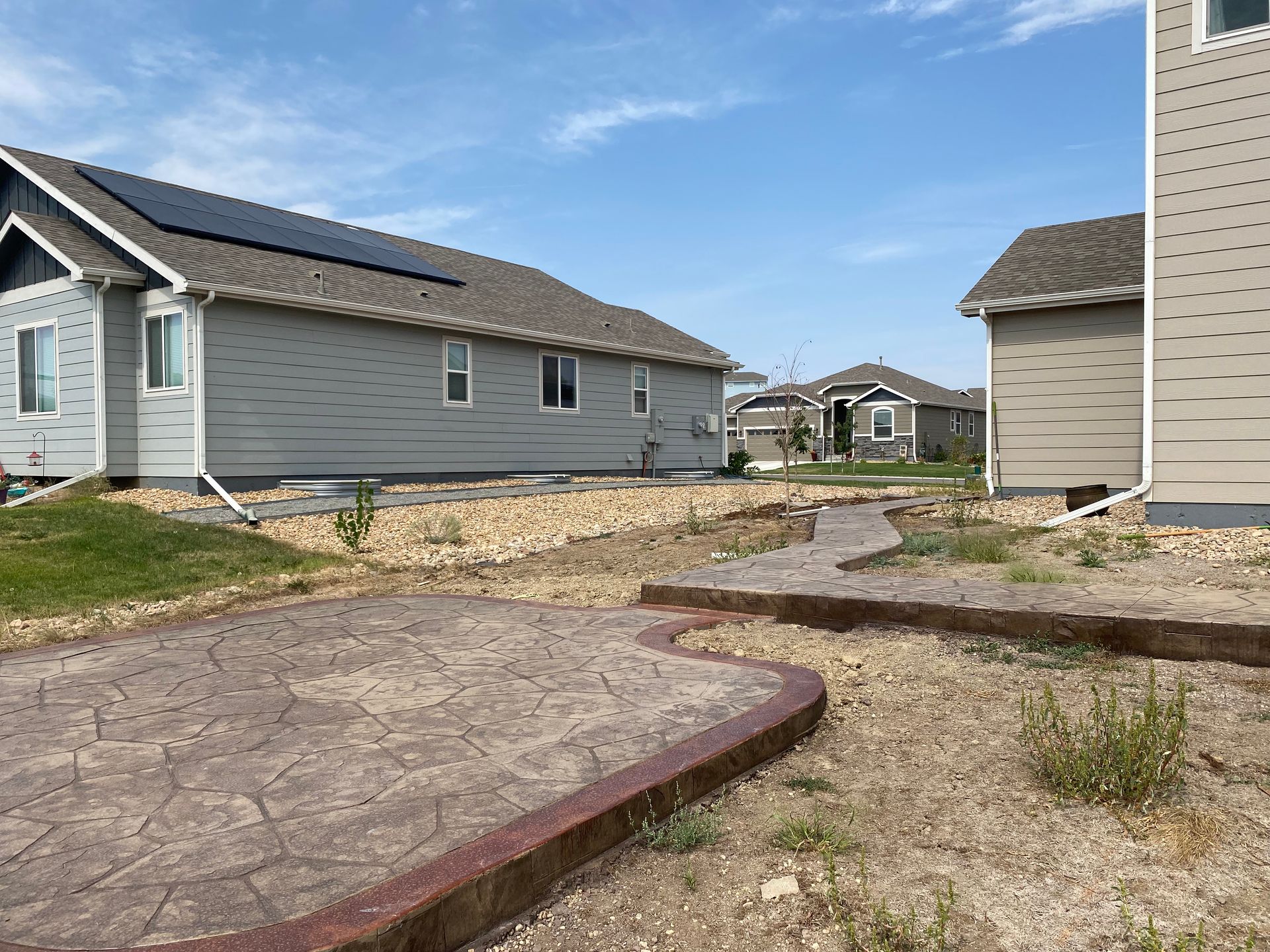 A backyard with a stone path, patio, and houses under a partly cloudy sky.
