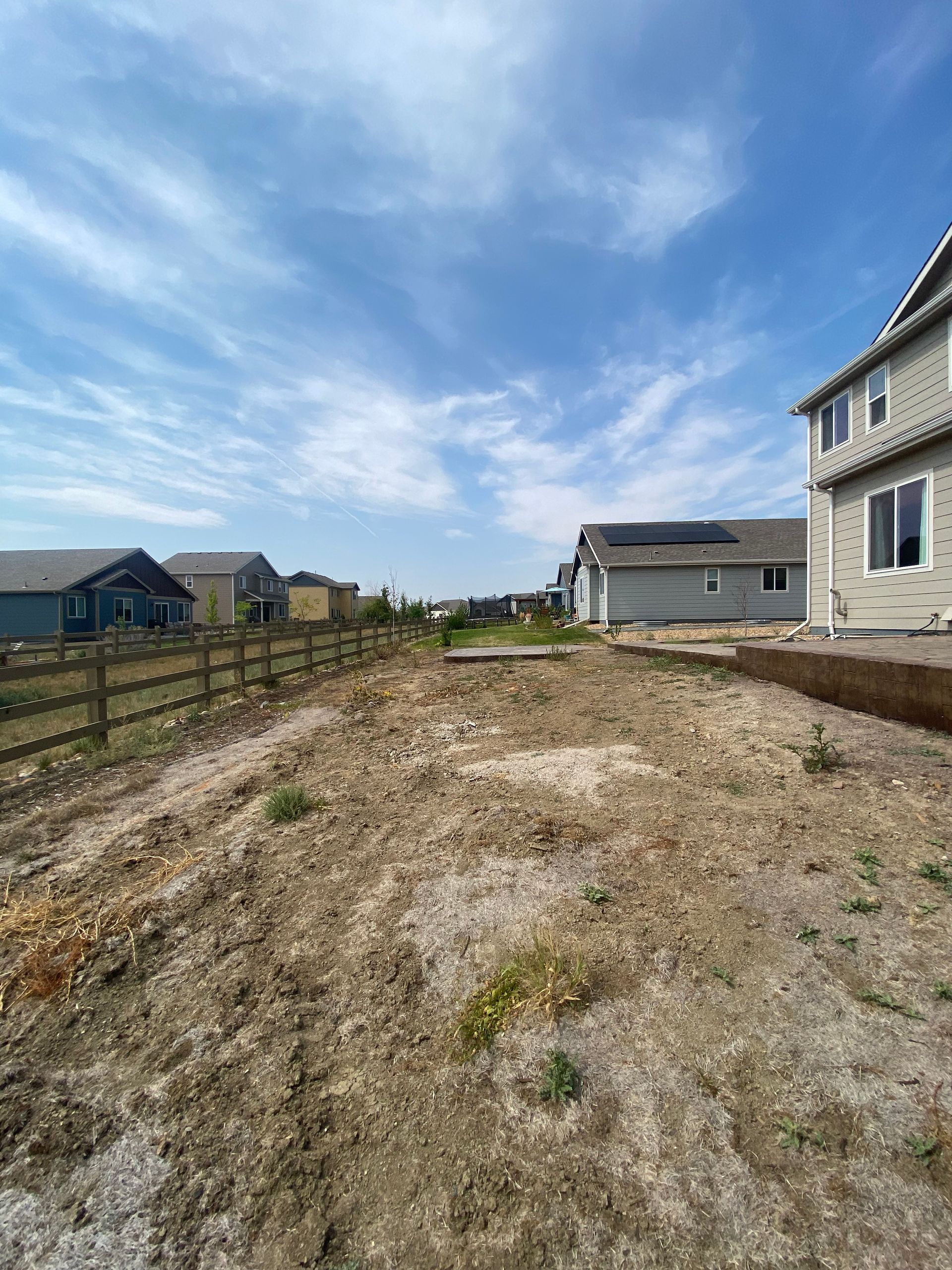 Dirt yard with a wooden fence, houses, and a blue sky with clouds.