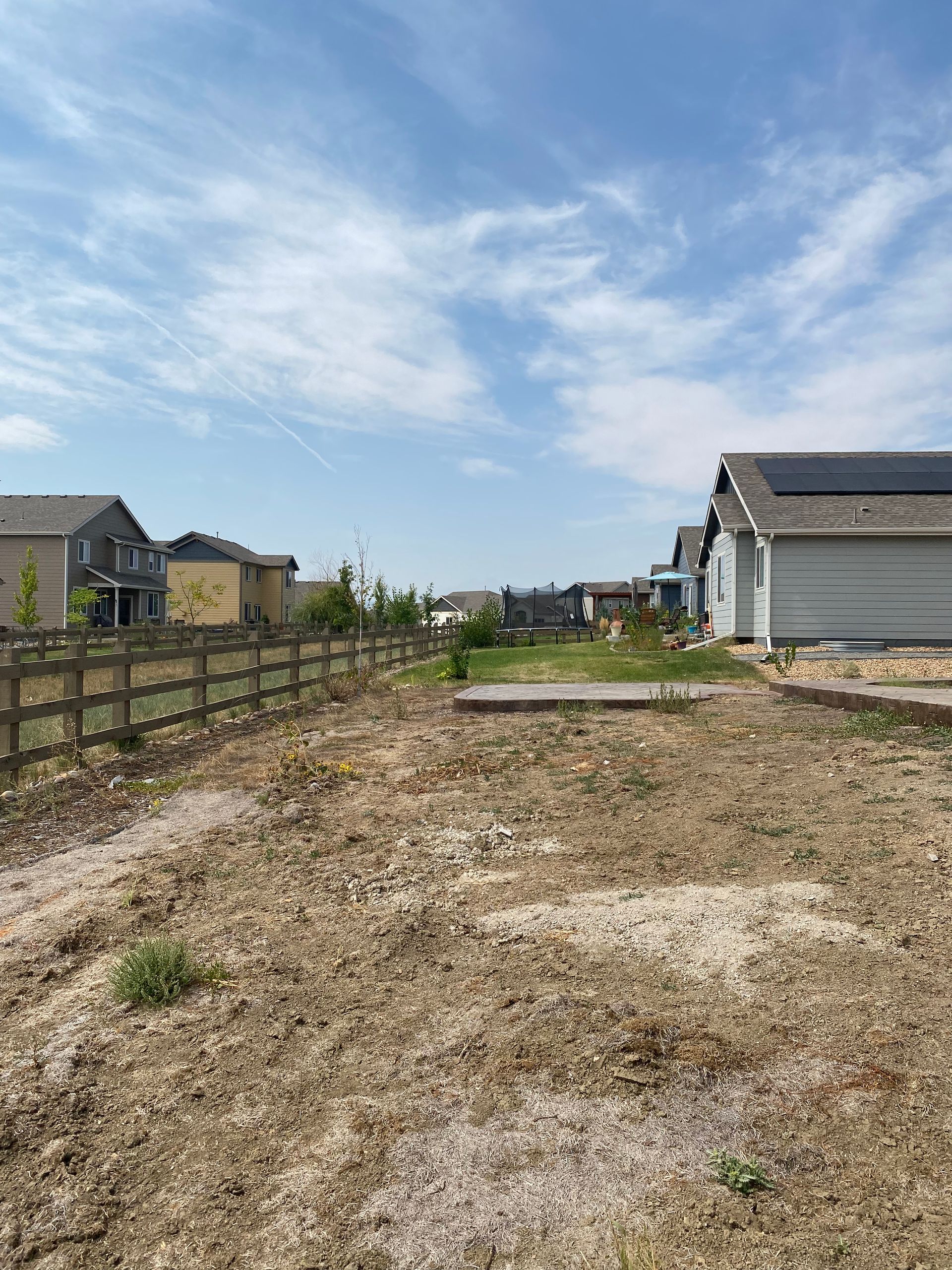 Dry backyard with a wooden fence, houses, and a clear blue sky.