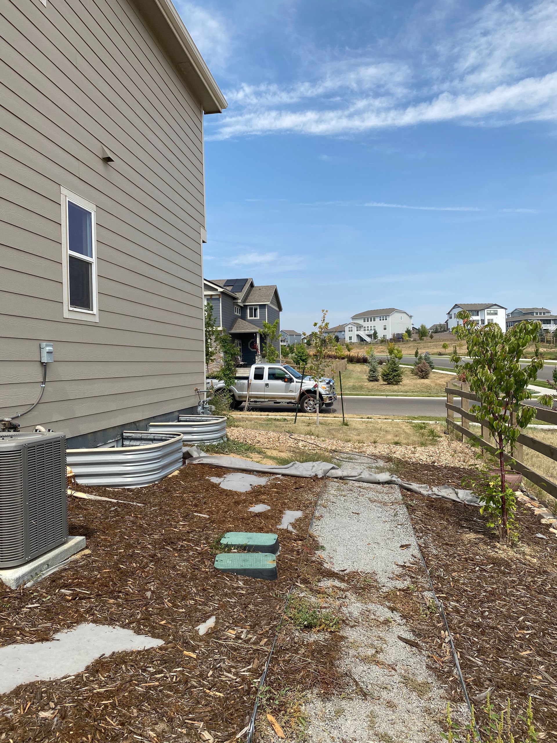 Side of a house with landscaping, a truck in the distance, and a sunny sky.