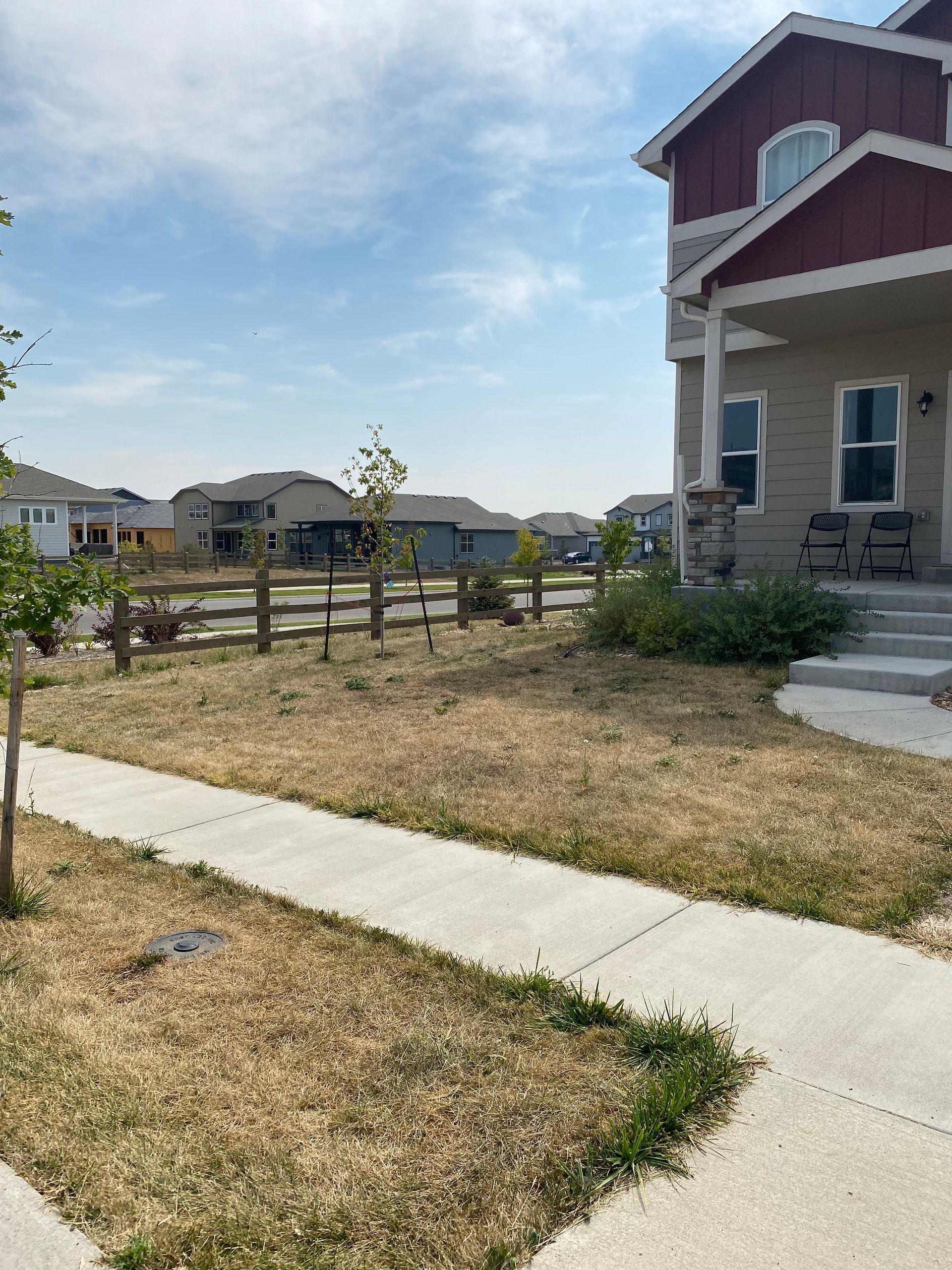 A two-story house with dry lawn. A sidewalk leads to the front door. Fence and other houses in background.