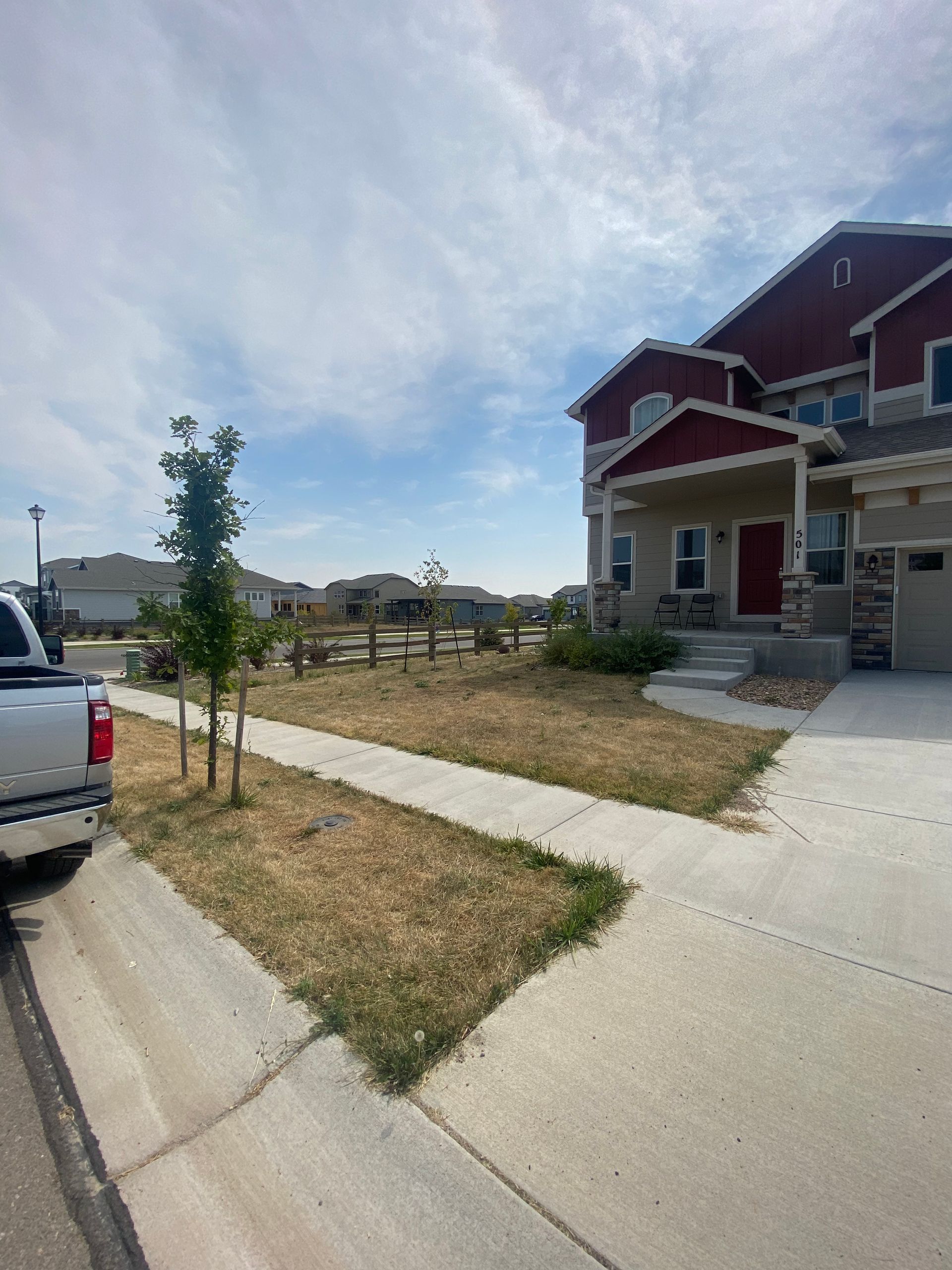 A house with red trim, a dry lawn, and a sidewalk on a sunny day.