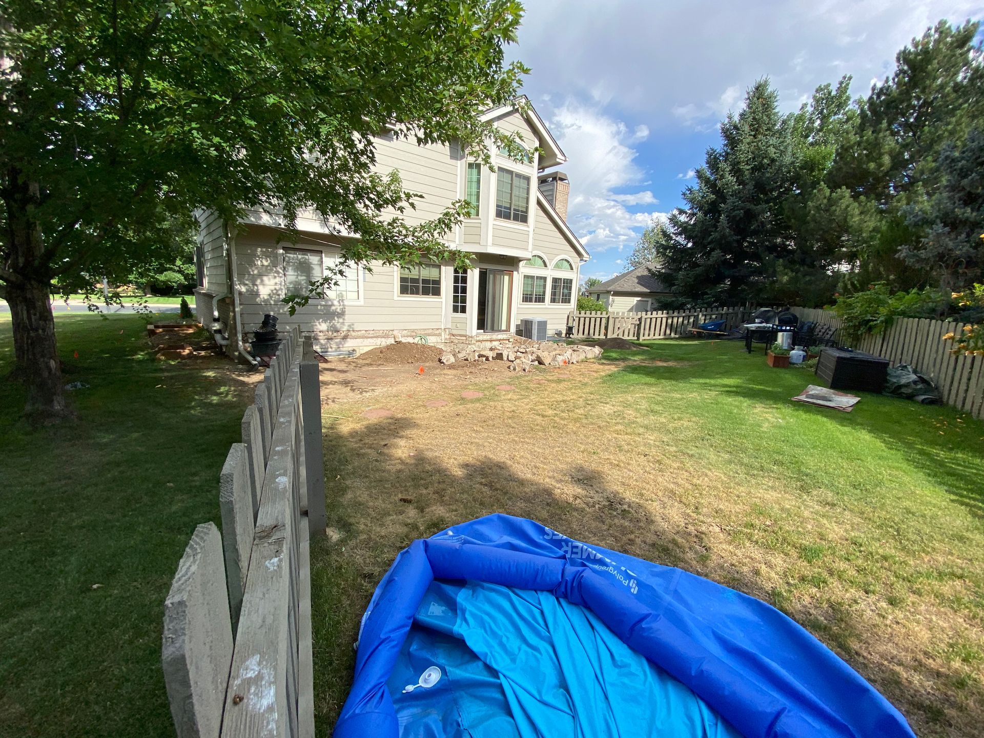 Backyard scene with a house, dry grass, a blue inflatable pool, and a wooden fence.