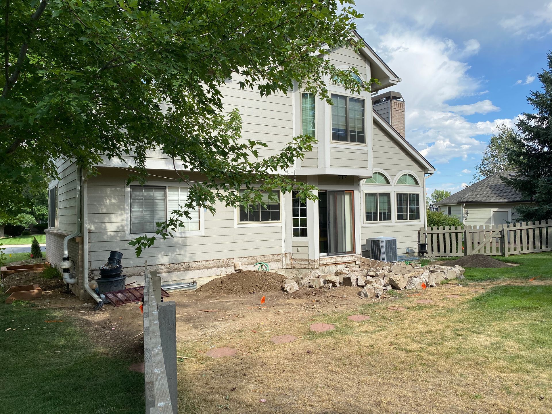 Backyard with a house, a pile of rocks, and a fence. The ground is dirt and grass.