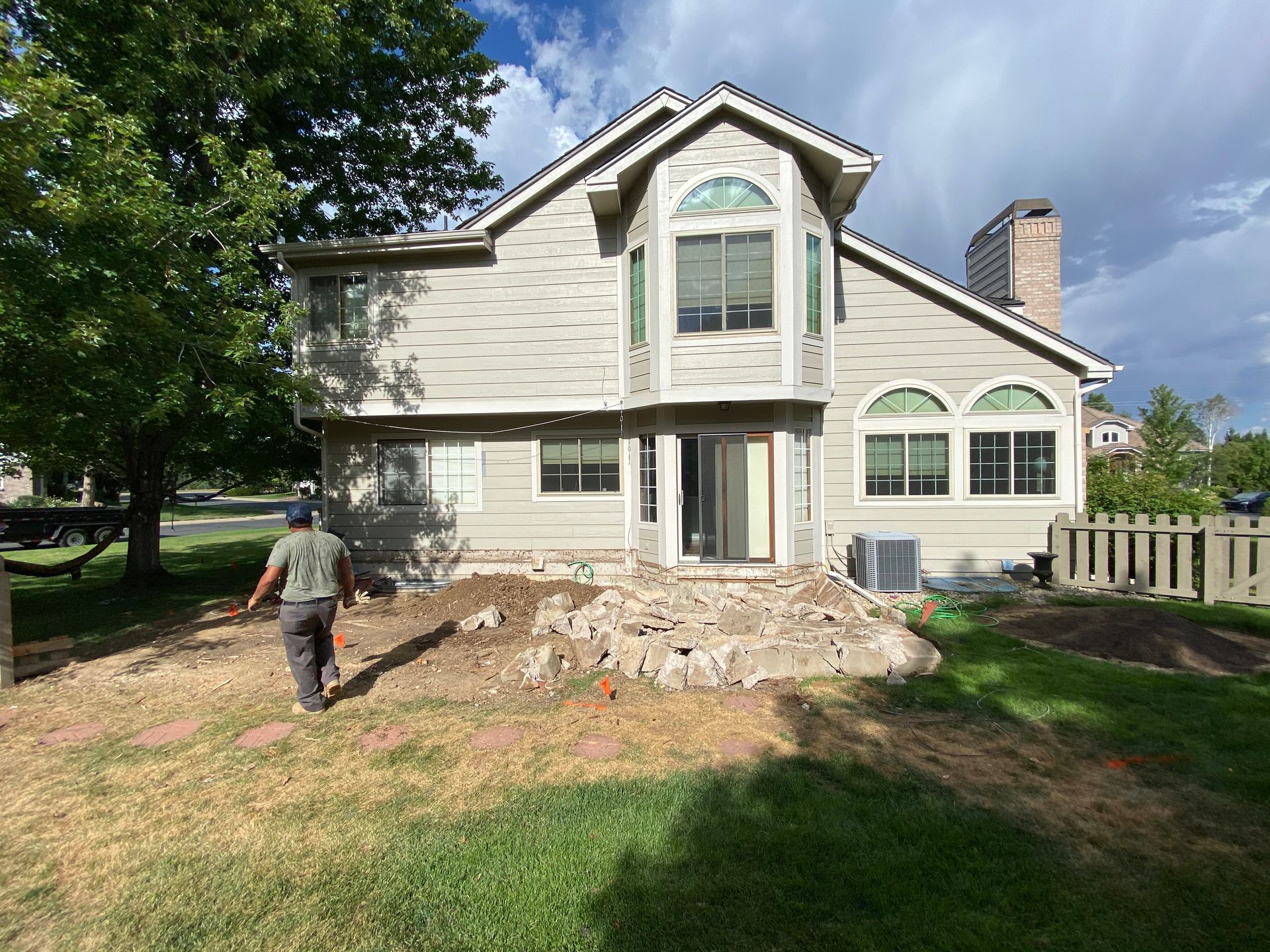 Man walks away from a house with a demolished patio in a backyard with grass and trees.