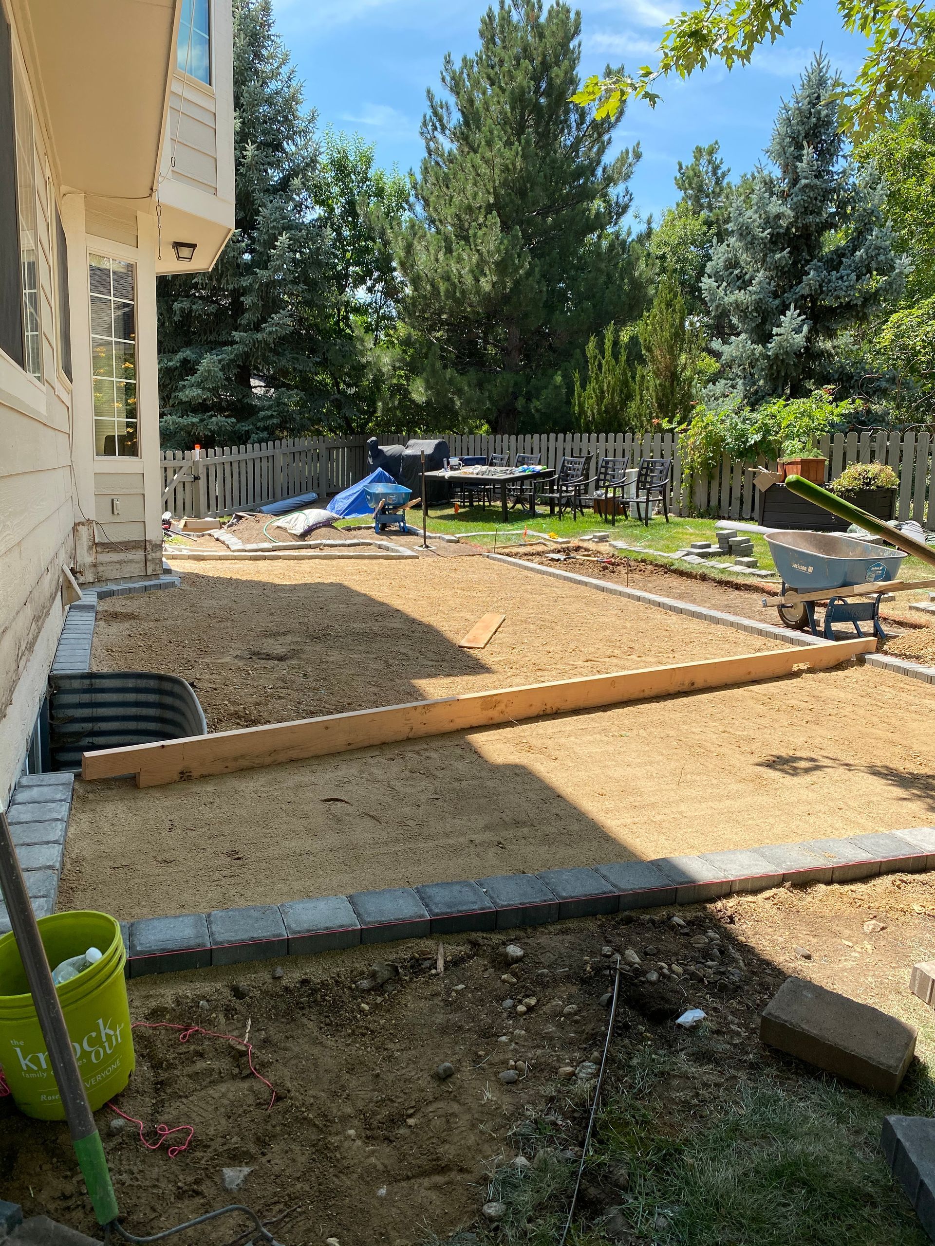 Backyard with gravel ground, wooden beam, and brick border; building at left.