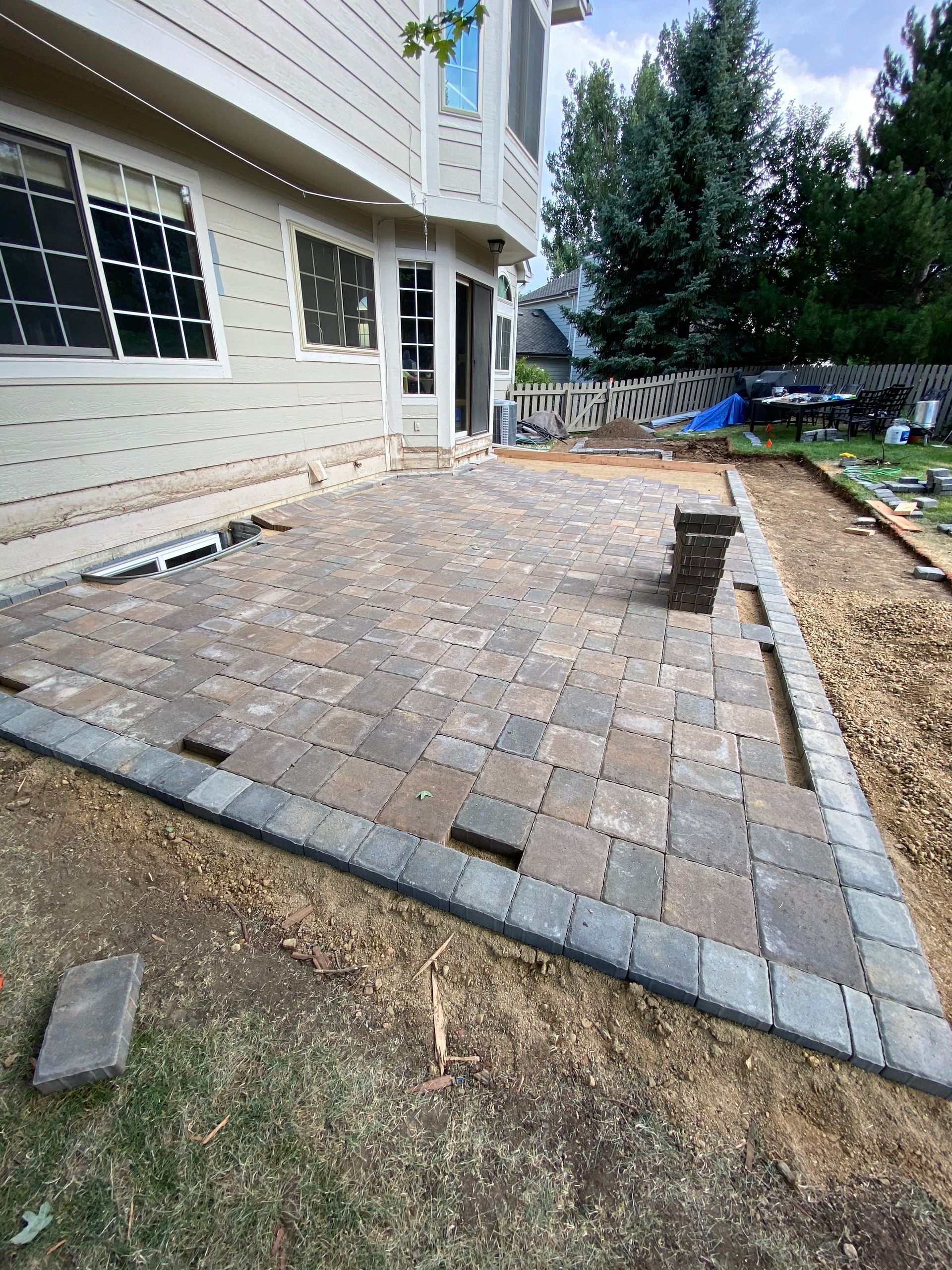 Patio being constructed with pavers near a house. Ground is partially covered with gravel.