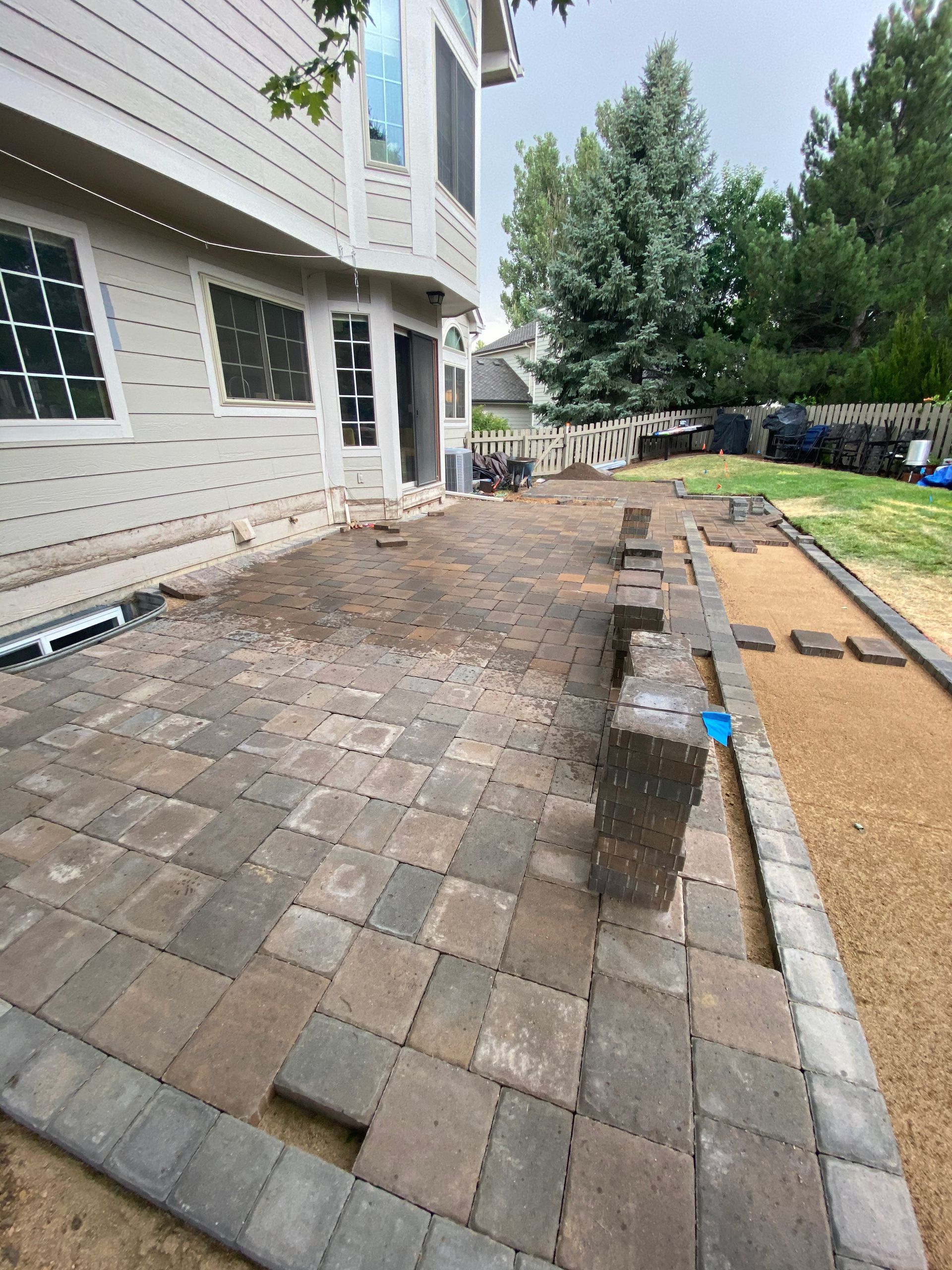 Patio construction: paving stones laid next to a house, with materials and unfinished areas.