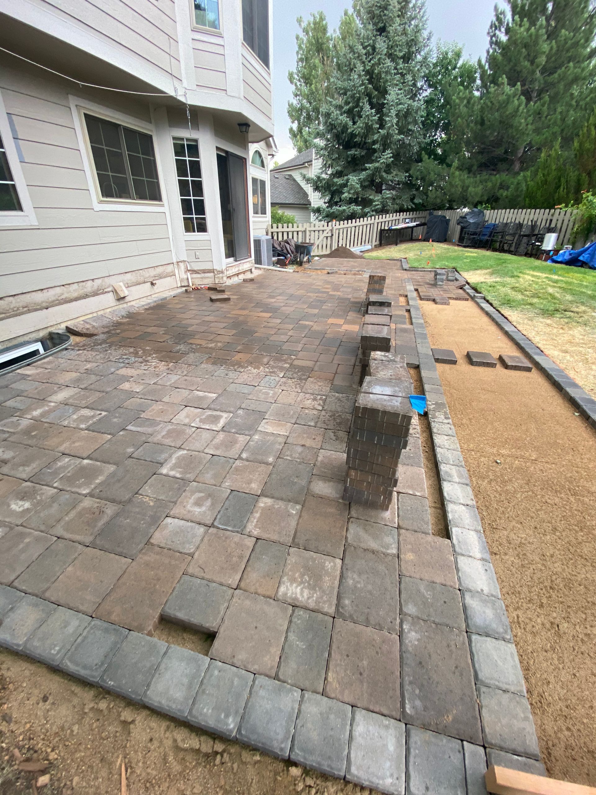 A patio under construction; grey pavers are being laid.