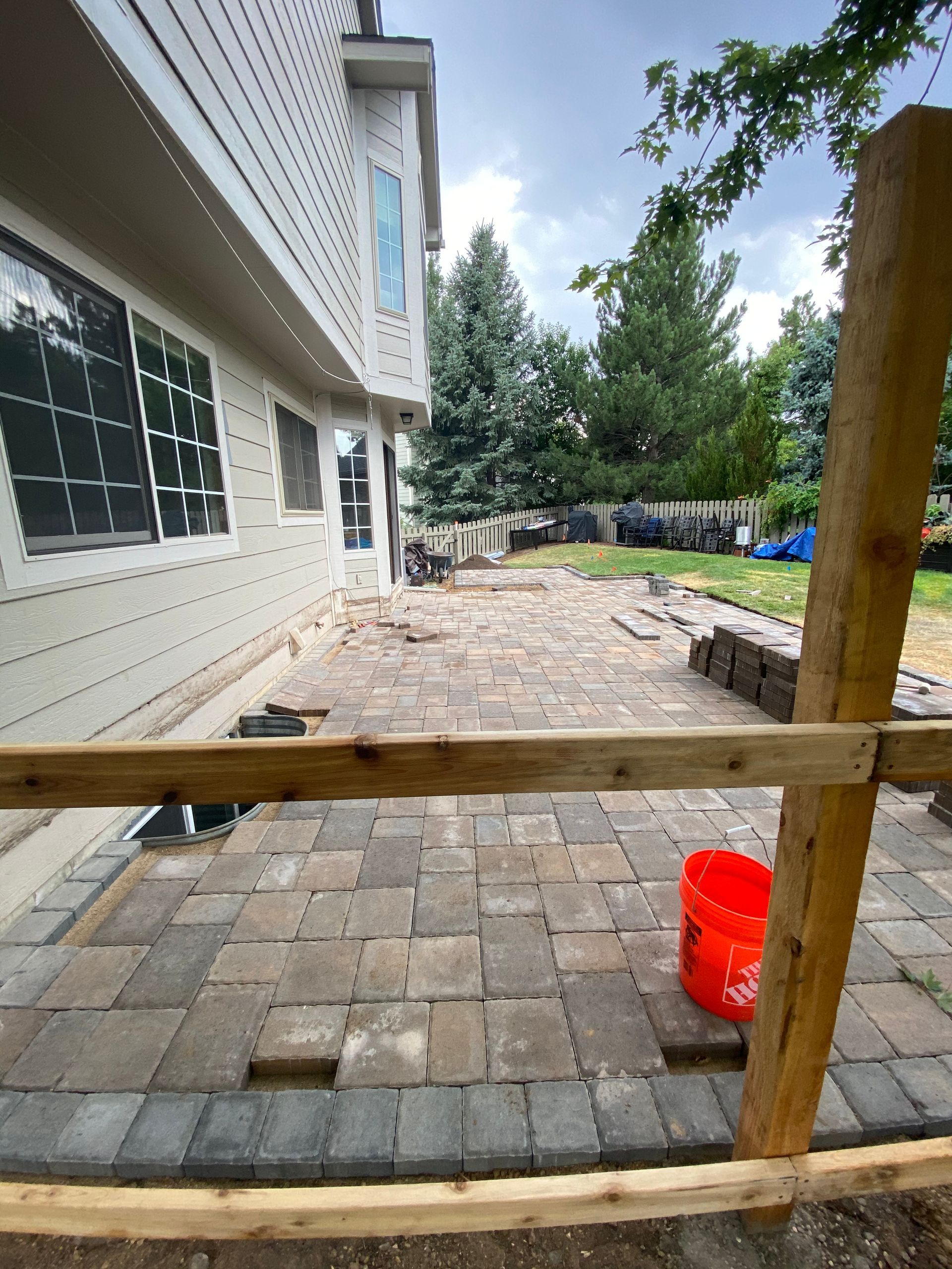 A patio is being built with pavers next to a house, an orange bucket sits on the patio.