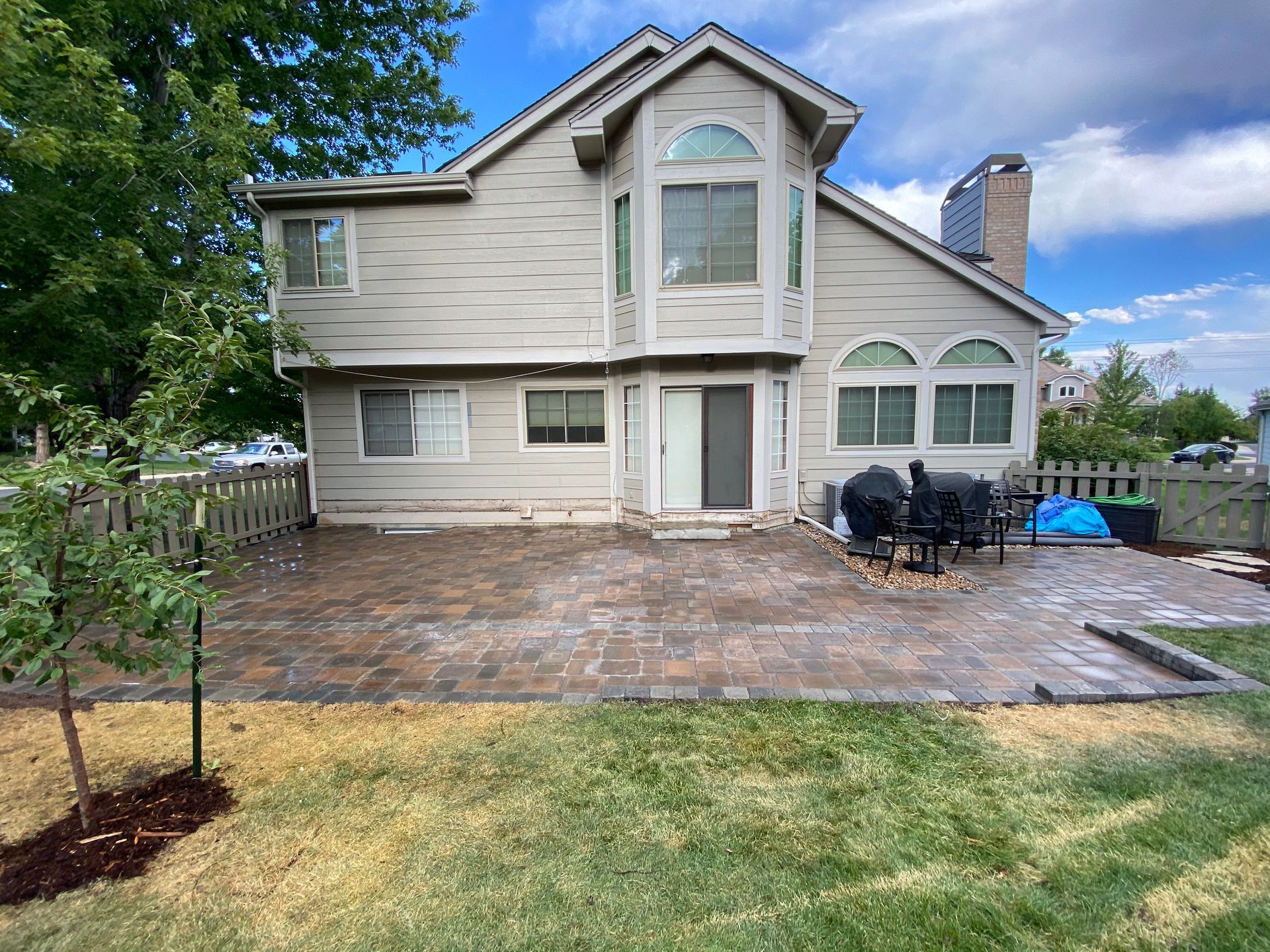 Backyard patio with a house, paver stones, grass, and a grill.
