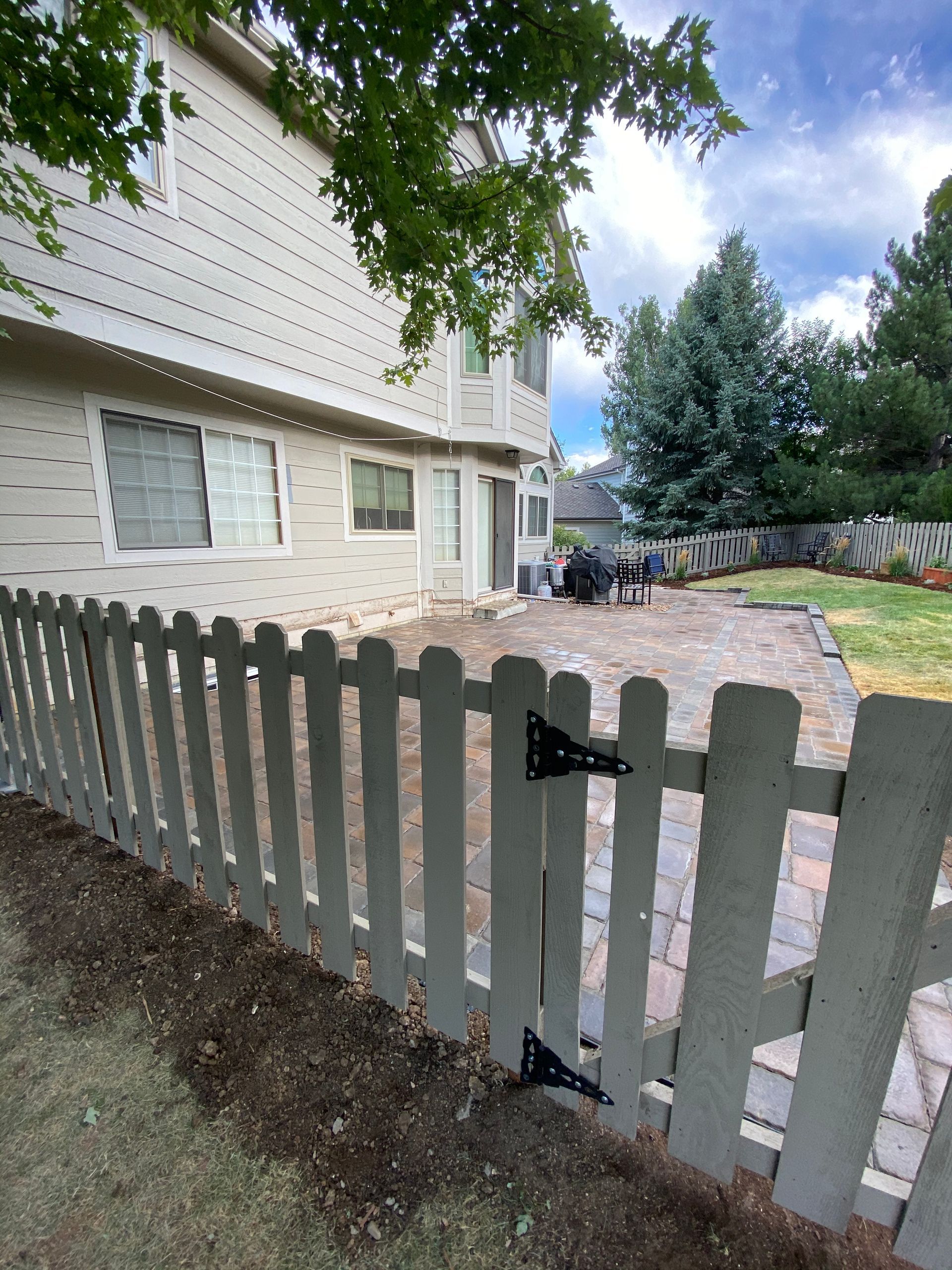 Beige house with a picket fence in front of a brick patio; blue sky.