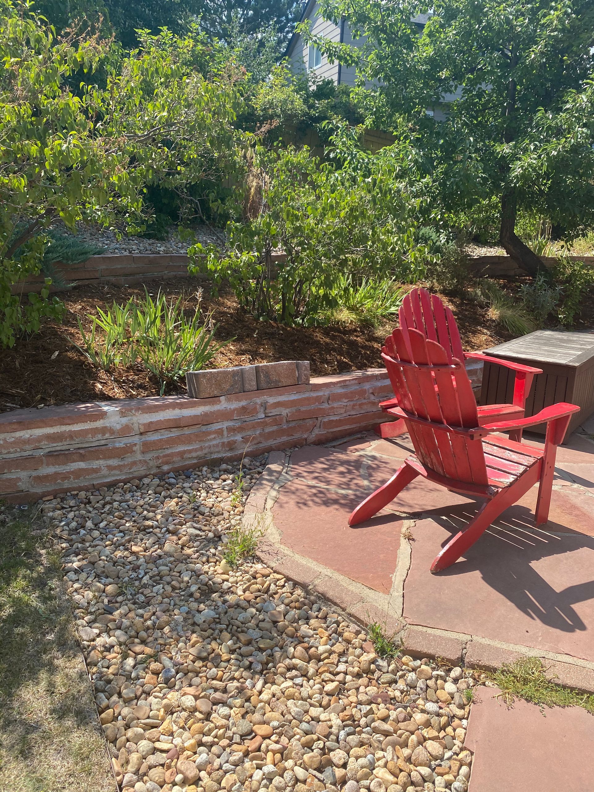 Red Adirondack chair on a patio with a brick wall and a hillside garden.