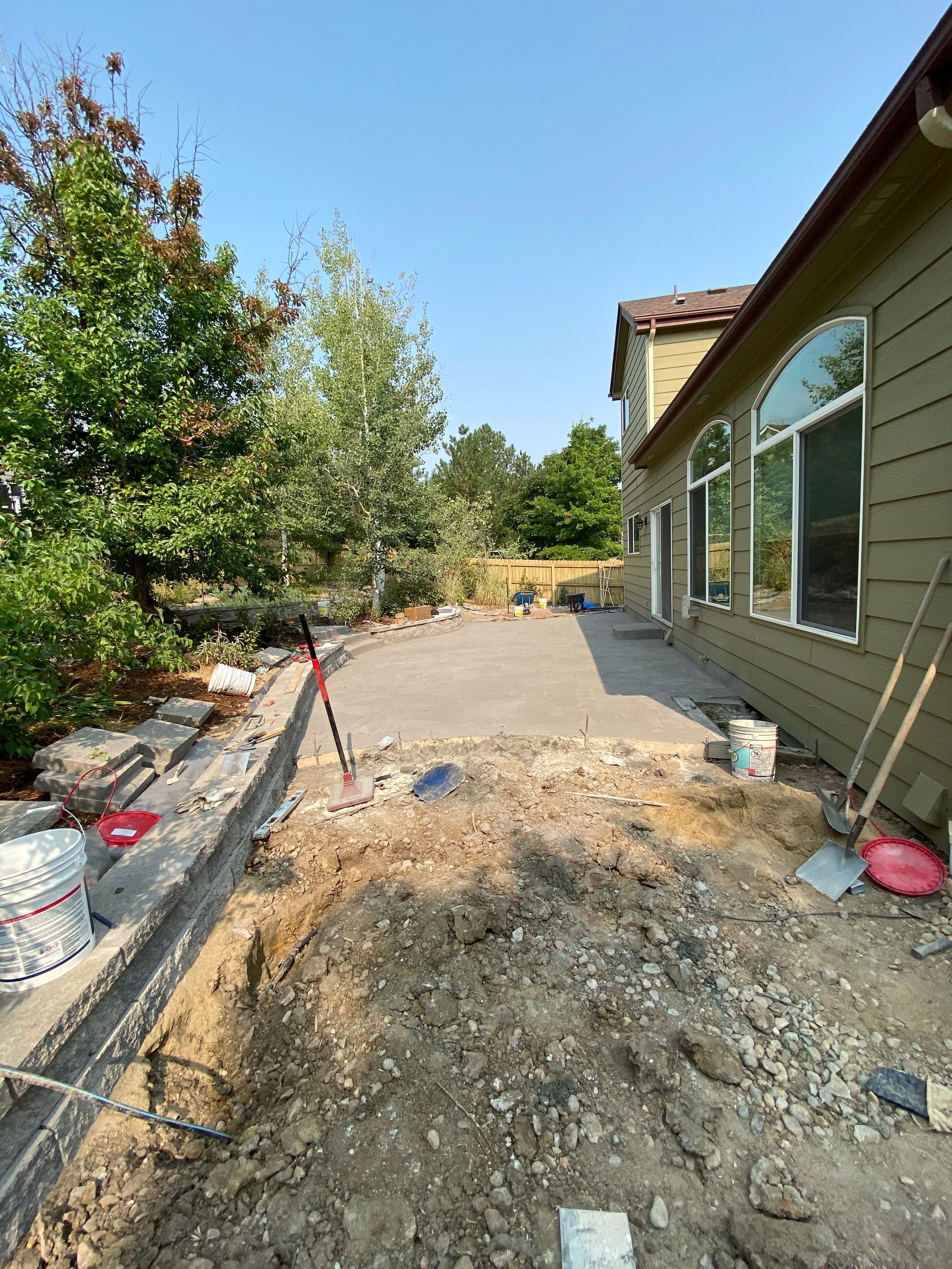 Construction site with a concrete patio, dirt, tools, and a house.
