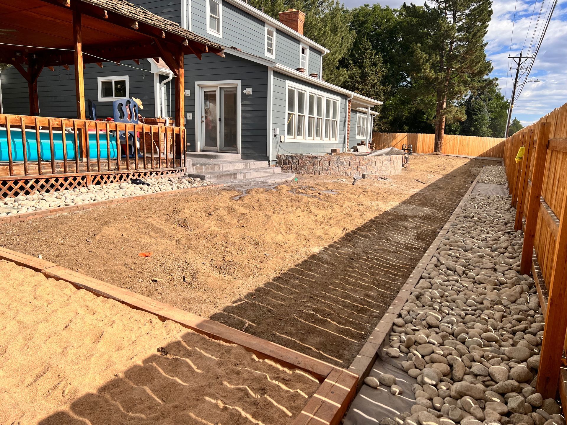 Backyard with gravel path, raised garden beds, wood fence, and blue house.